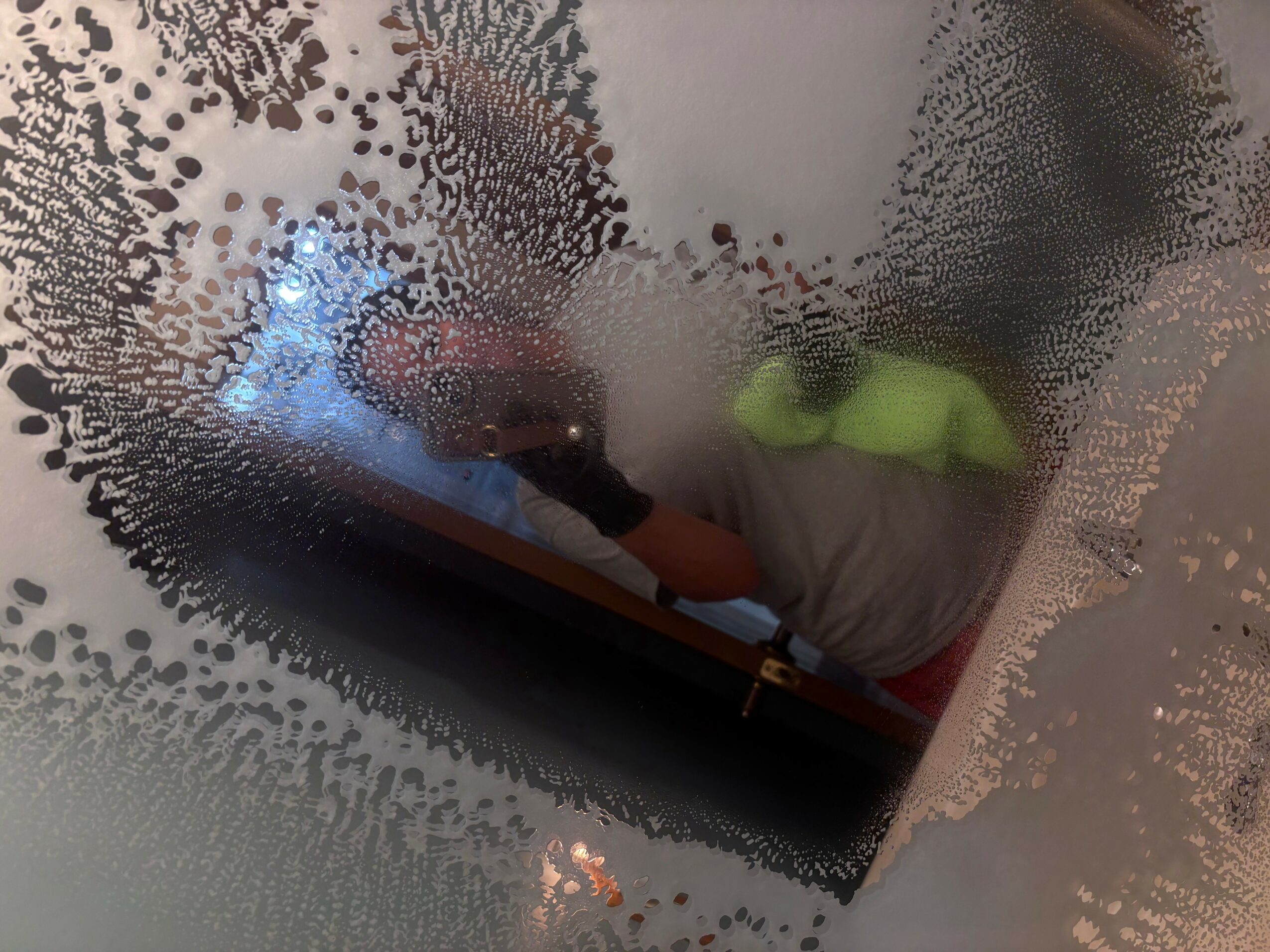 Person in a gray shirt and green hat seen through a foggy or wet glass surface, obscuring details.