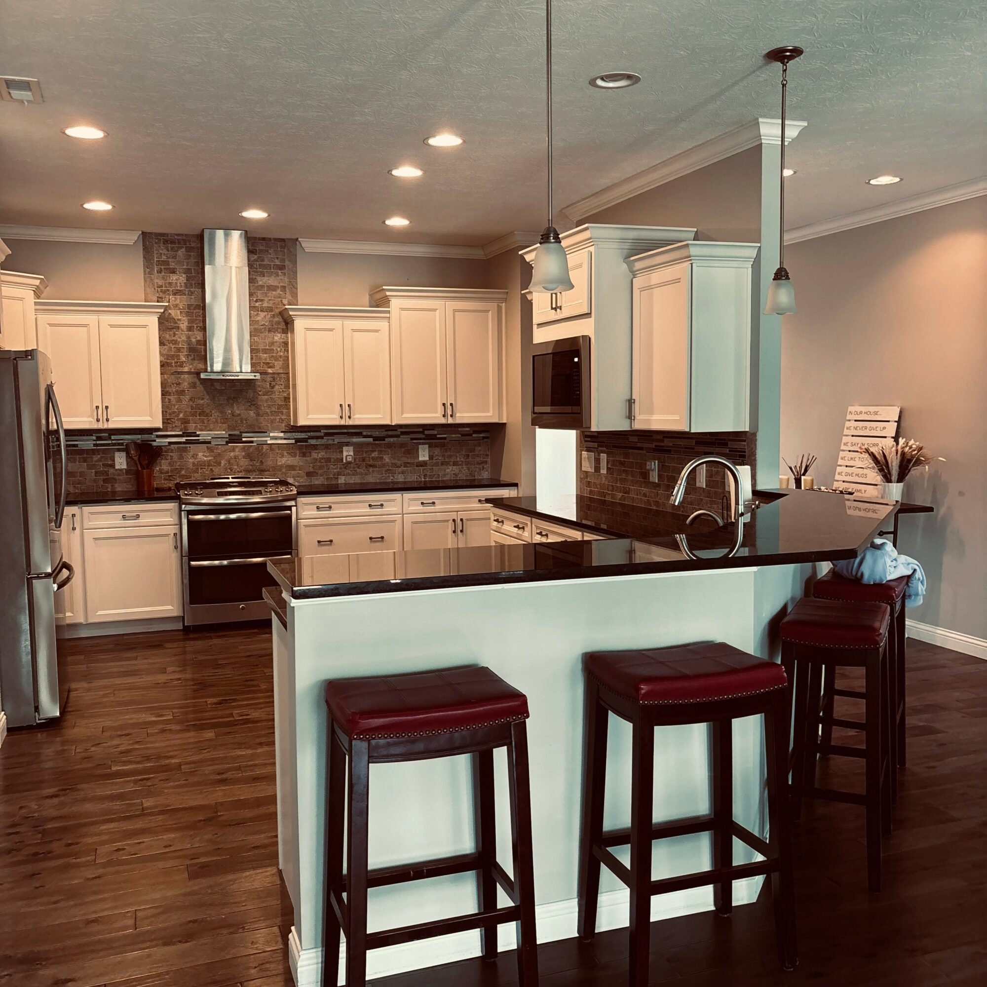 Kitchen with white cabinets, black countertops, and a brick backsplash. Three bar stools are at the counter, with pendant lights above.