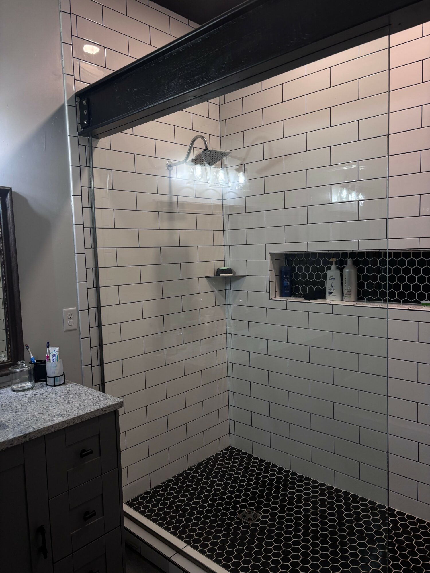 Bathroom shower area with white tiled walls, a showerhead, and a small shelf, viewed from outside the shower.