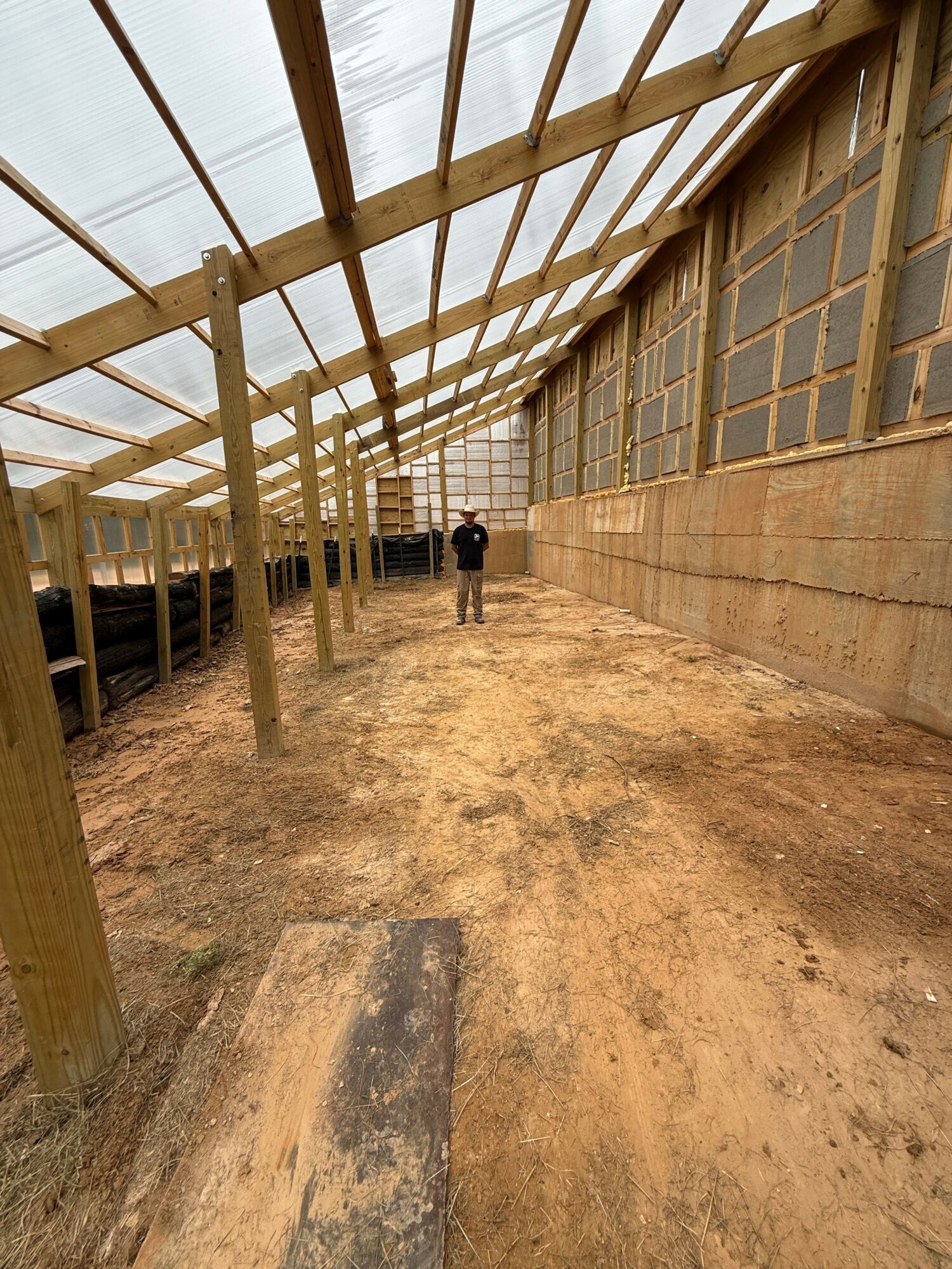 Construction site with wooden framework and dirt floor, partially covered with plastic sheeting, viewed from the side.