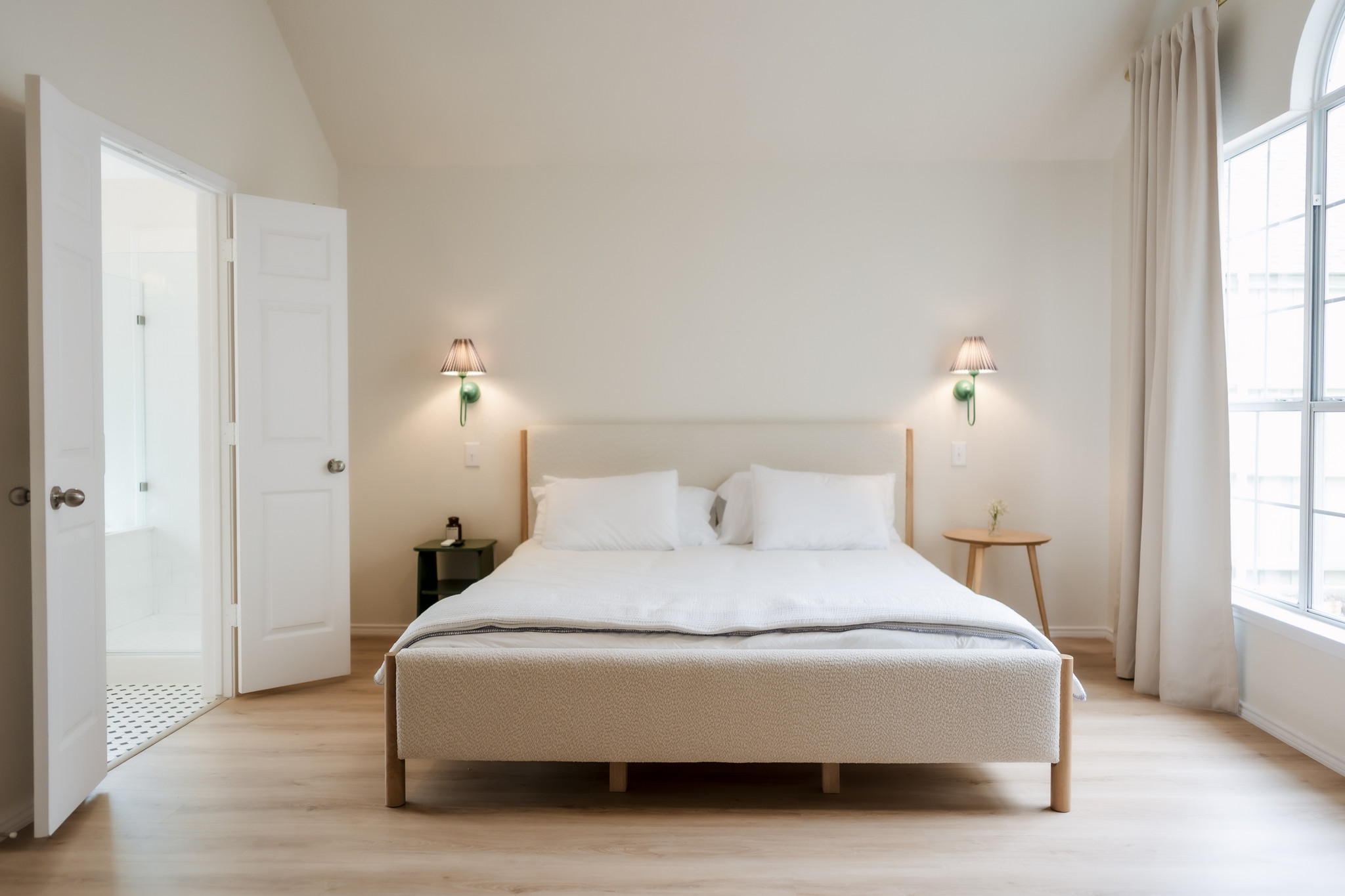 Upright bedroom with a bed, two wall-mounted lamps, and a large window with curtains.