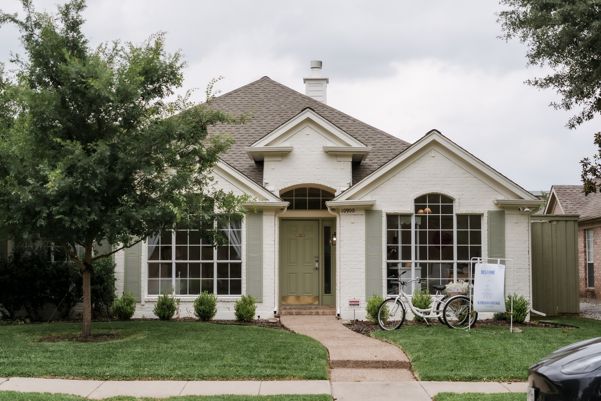 Front view of a white house with a green door, large windows, bicycles, and a lawn.