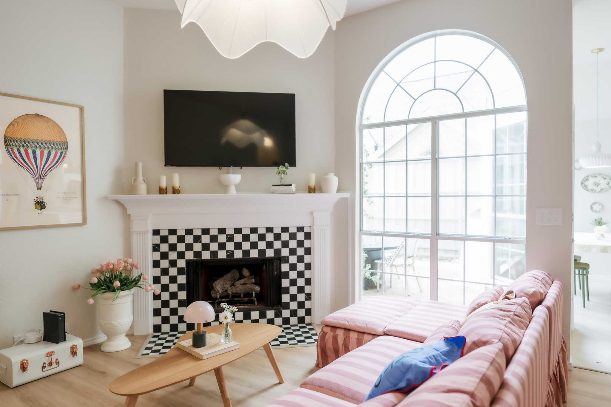Living room with a pink sofa, large window, fireplace, wall-mounted TV, and decorative items, bright and airy space.
