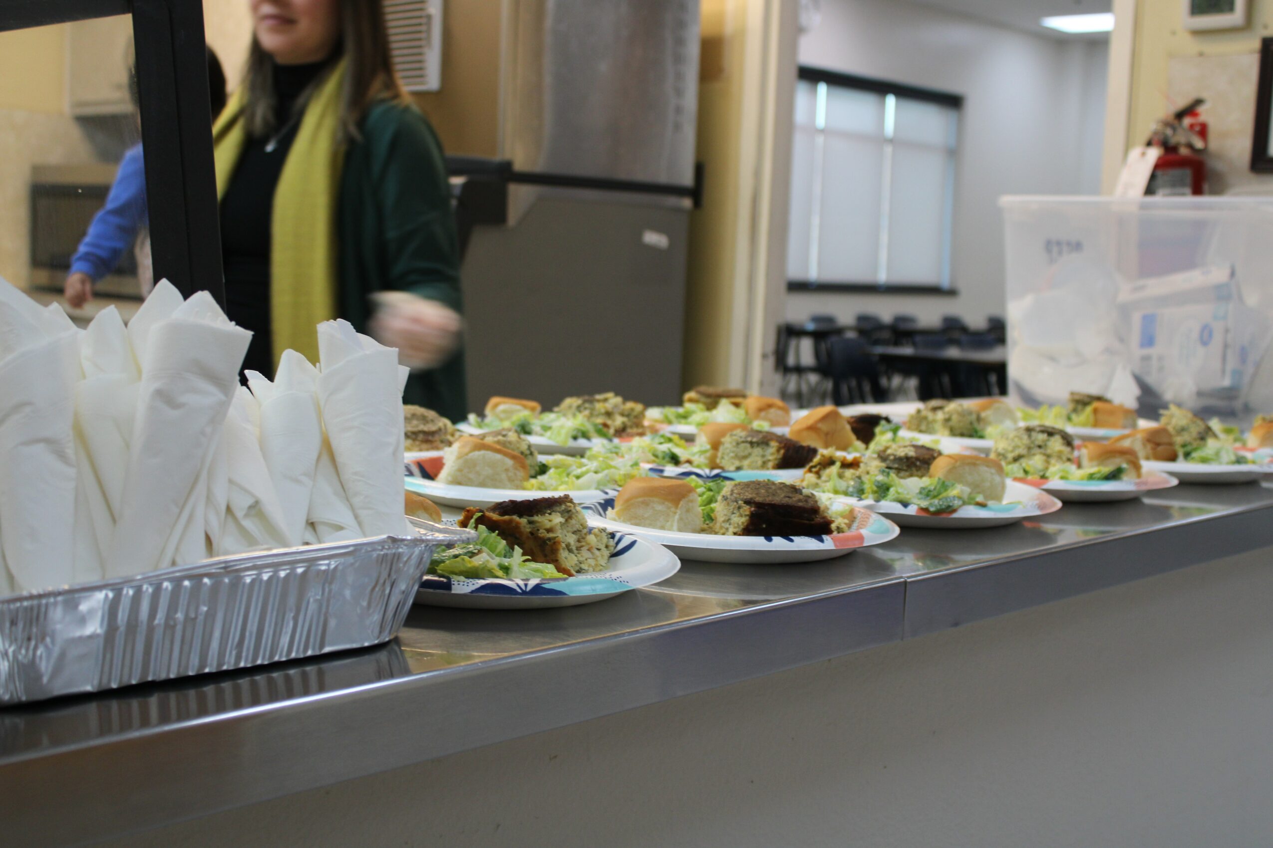 Several plates of sandwiches on a counter with a person in the background in an indoor setting.