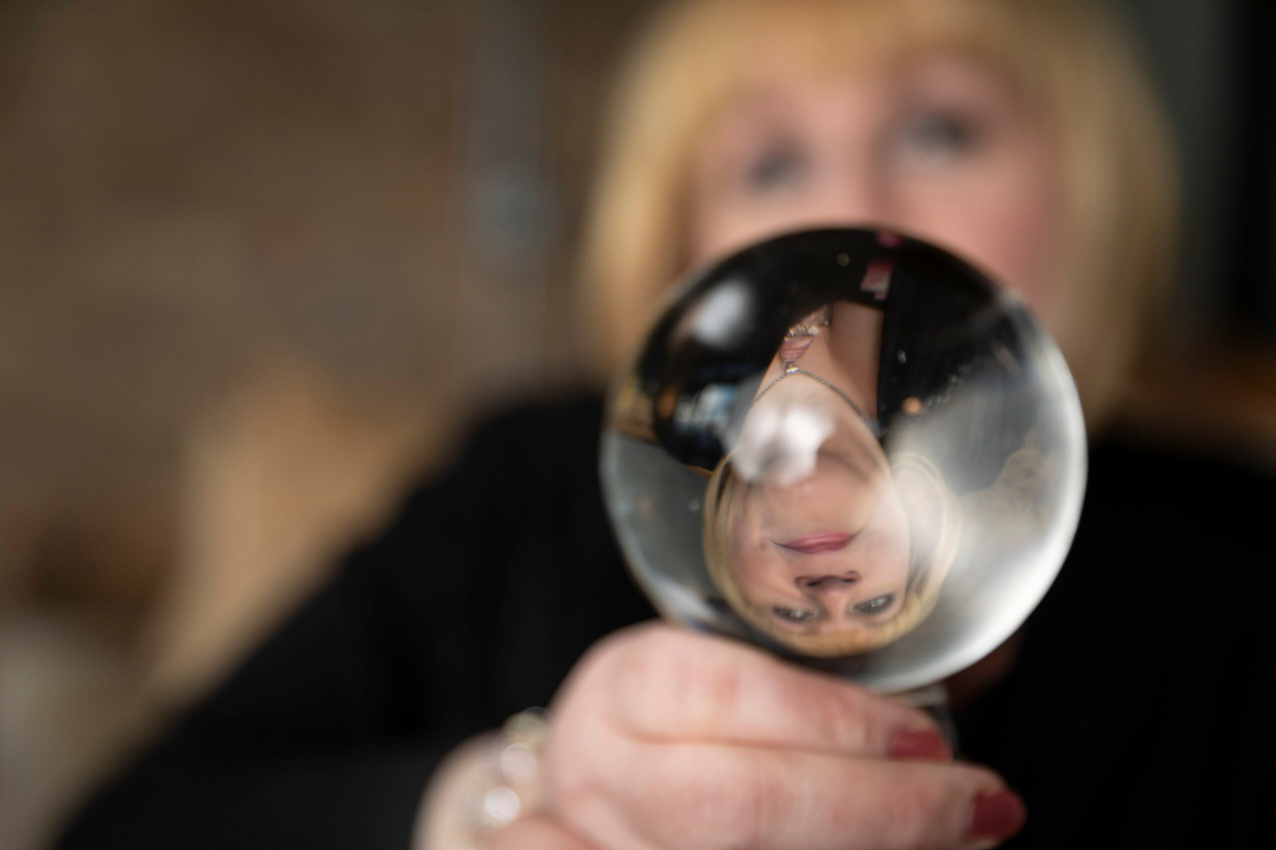 Person holding a glass with a reflection of their face, blurred background, face partially visible, focus on glass.