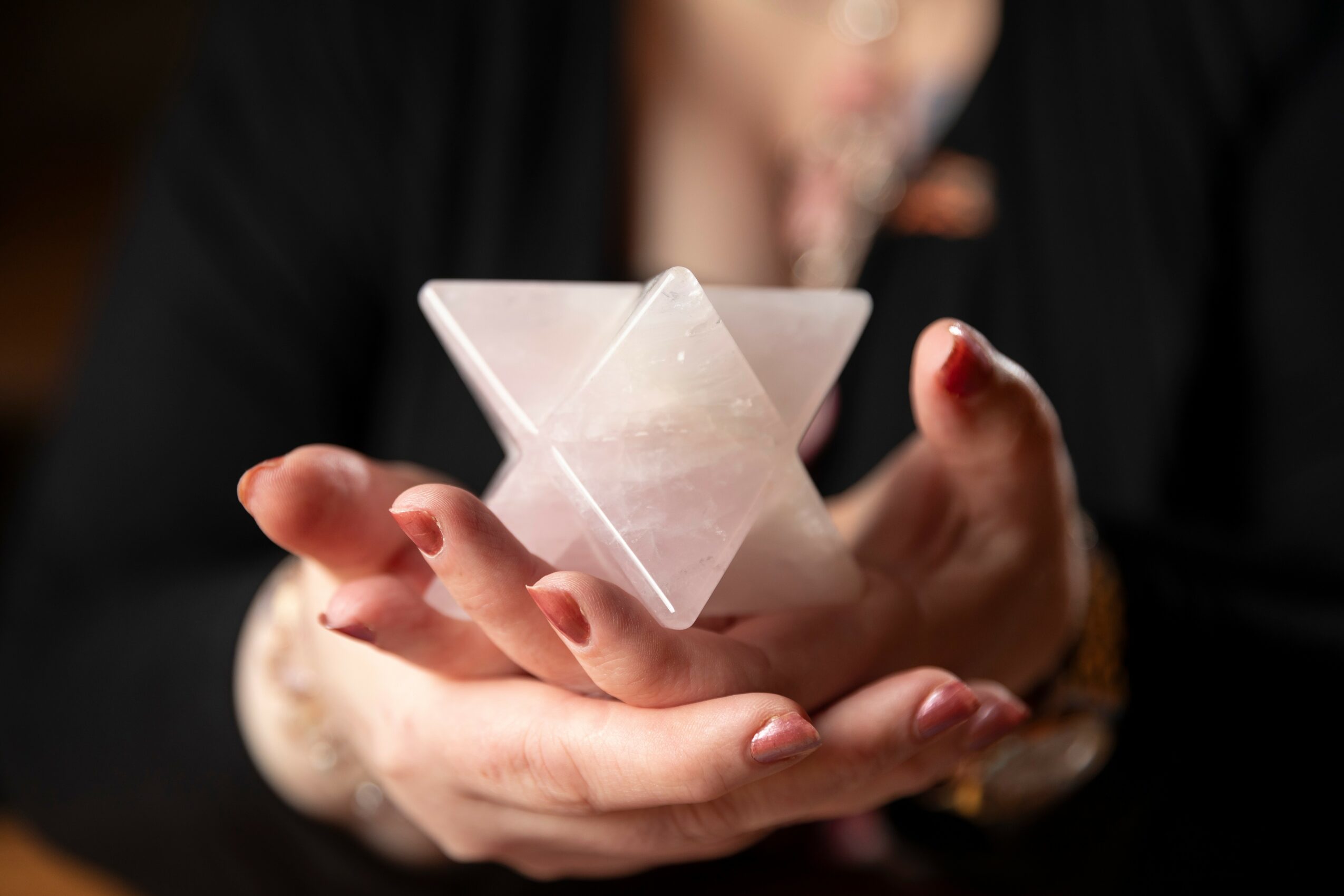 Person holding a translucent, geometric, pyramid-shaped object in their hands, with a blurred background.