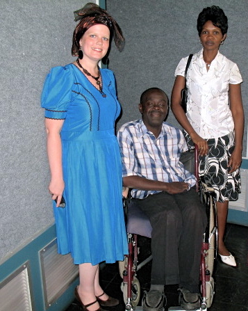 Three people, two women and one man in a wheelchair, pose indoors against a gray wall.