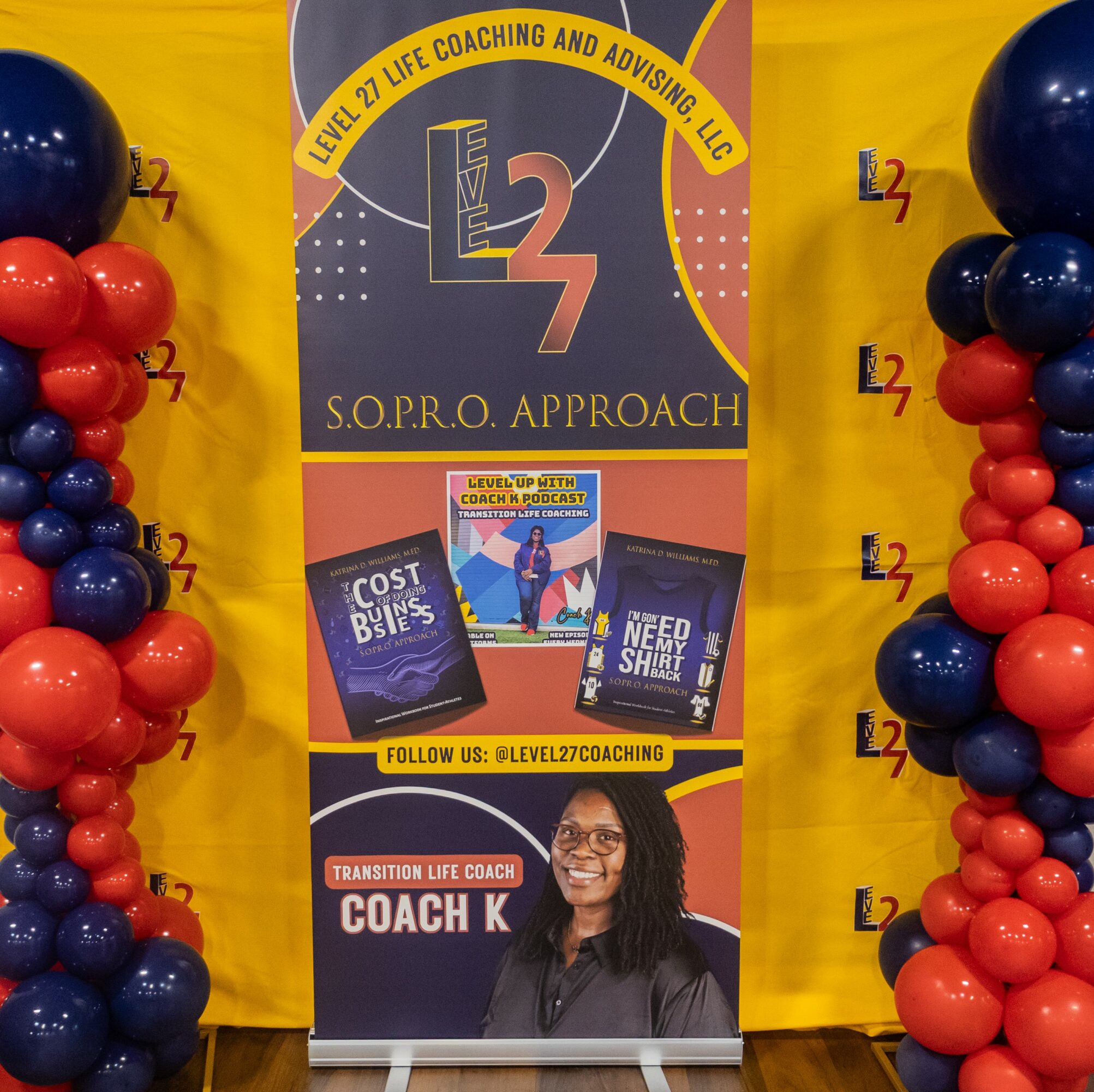 Display with banners and balloons promoting life coaching, featuring books and a woman smiling, on a yellow background.