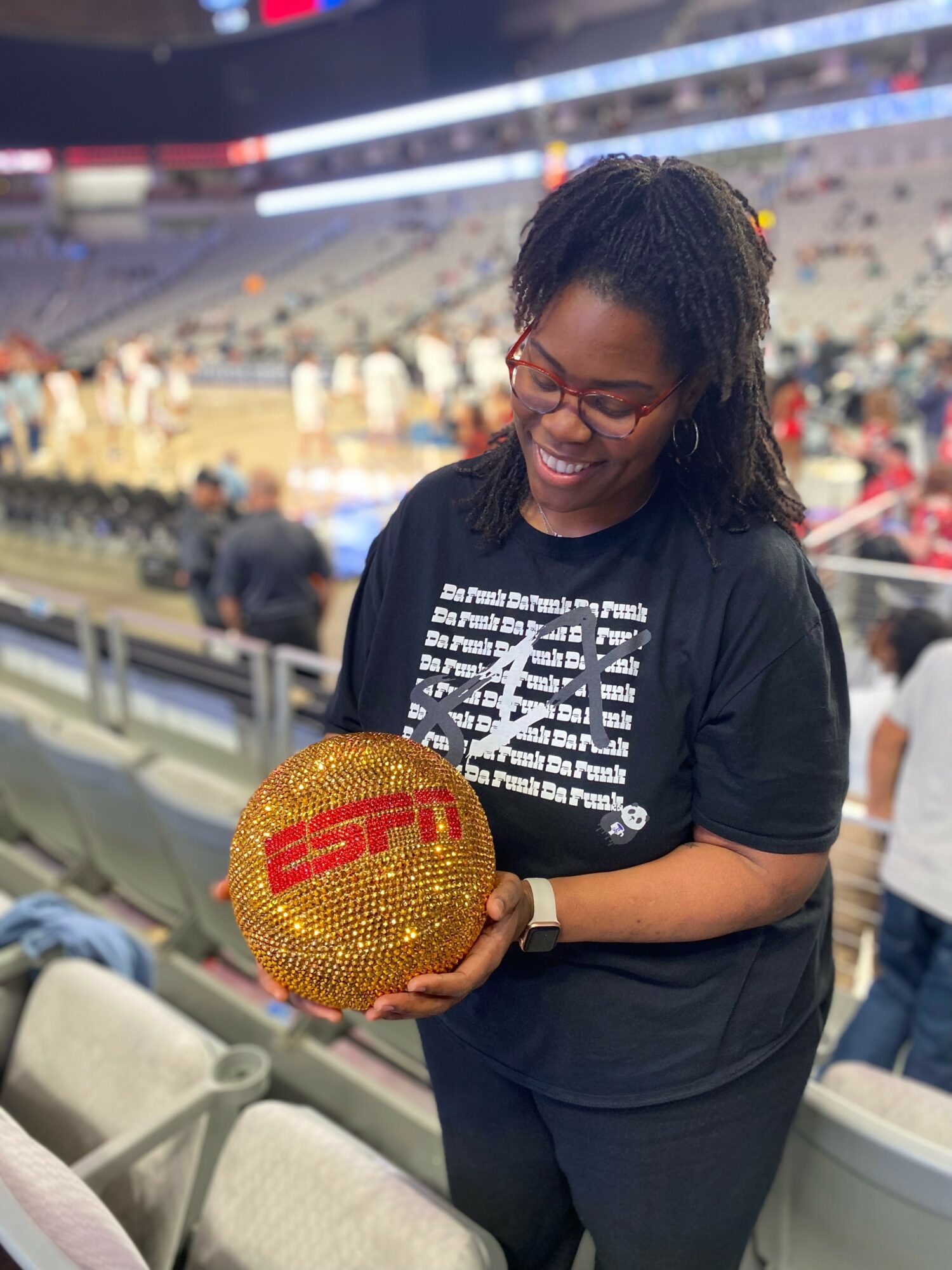 Woman smiling at basketball with ESPN logo, holding it in a stadium with empty seats in background.