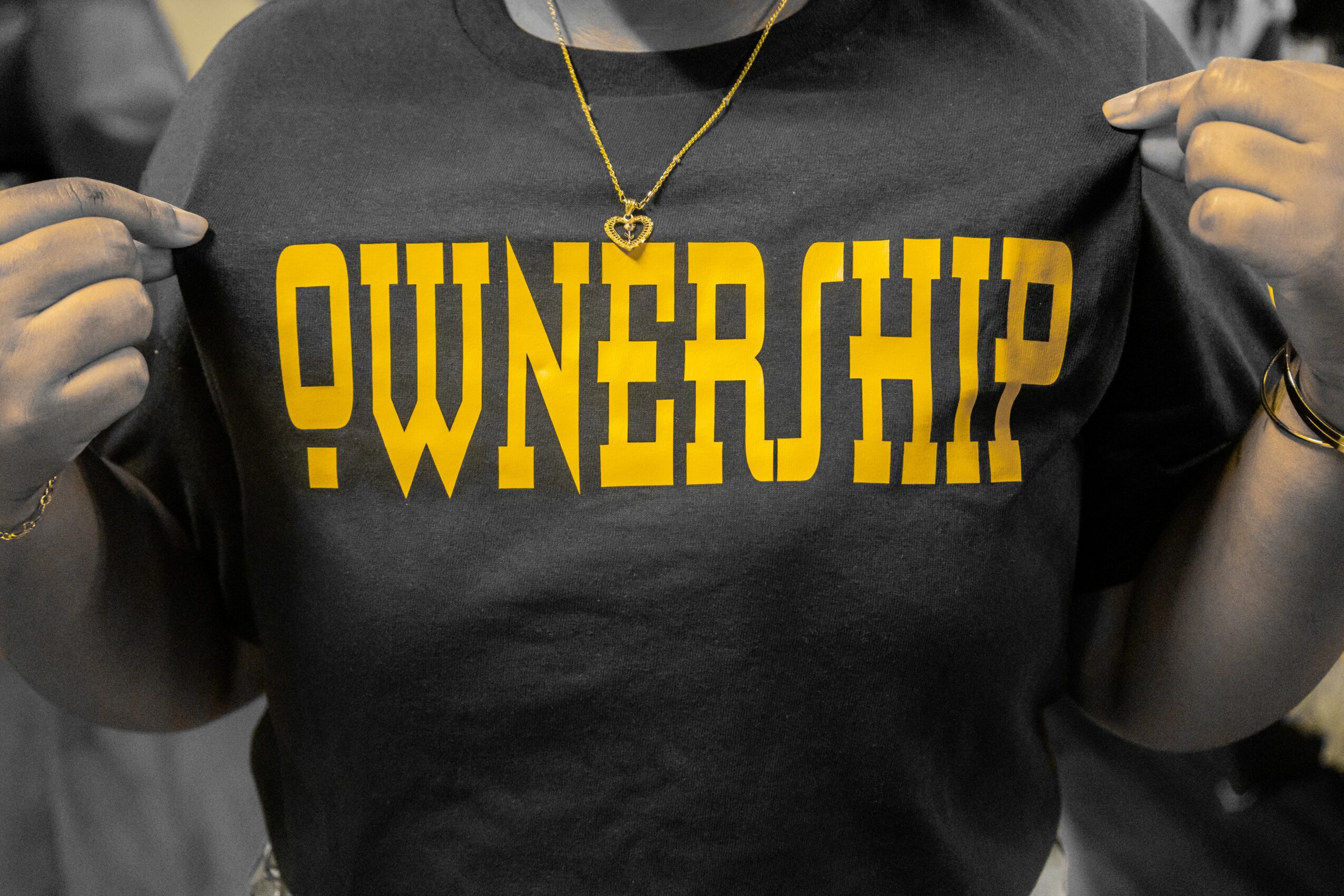 Person holding a black shirt with yellow text reading 'OWNERSHIP'.