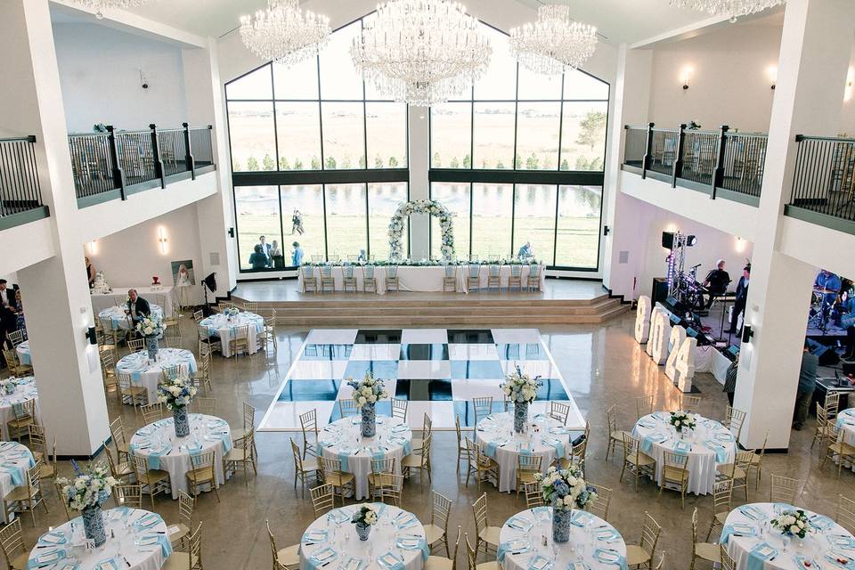 Elegant event space with round tables, floral centerpieces, large windows, and chandeliers, set for a formal gathering.