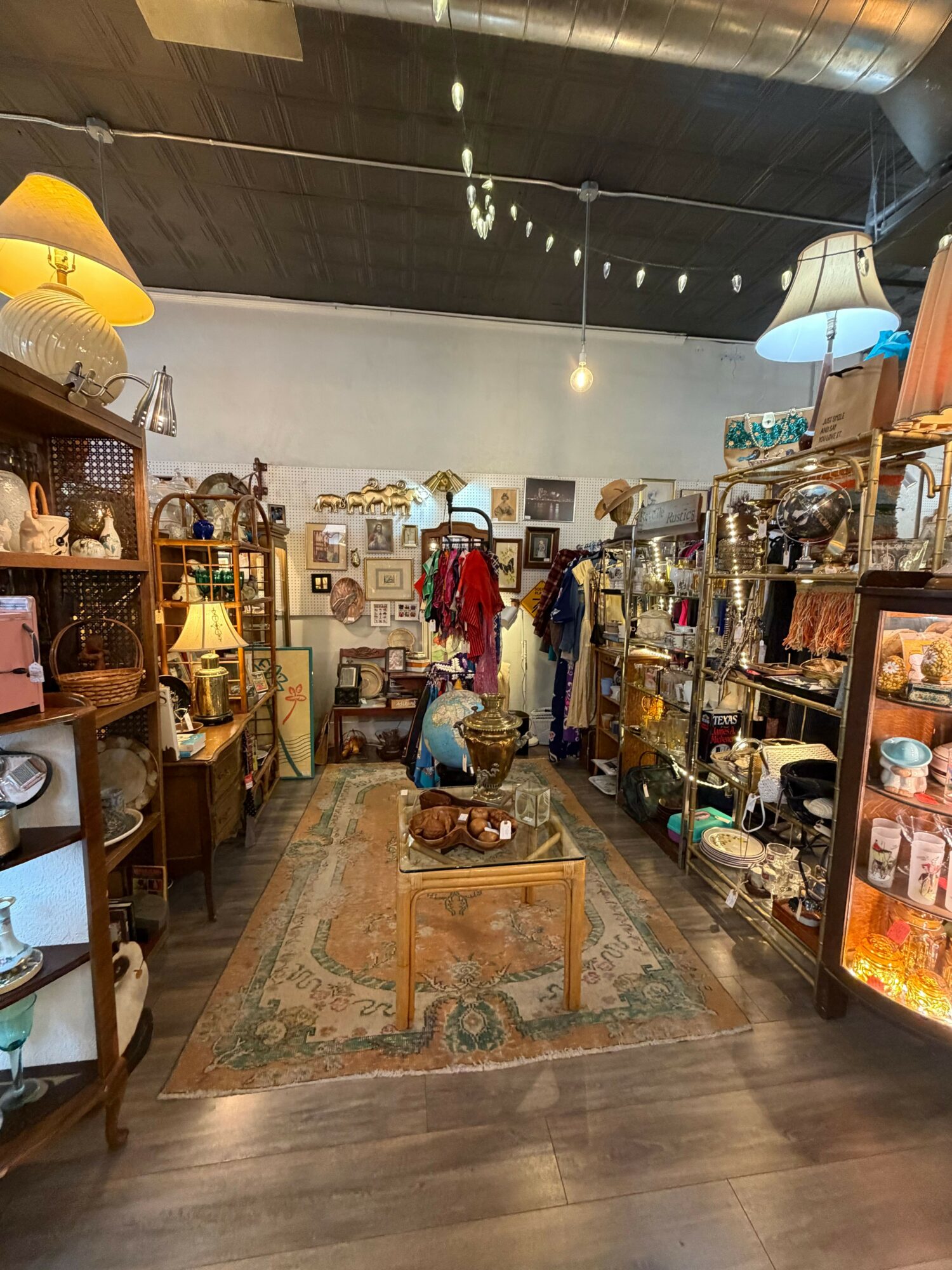 Interior of a store with shelves, furniture, and a person browsing, viewed from the side. Wooden floor and display items visible.