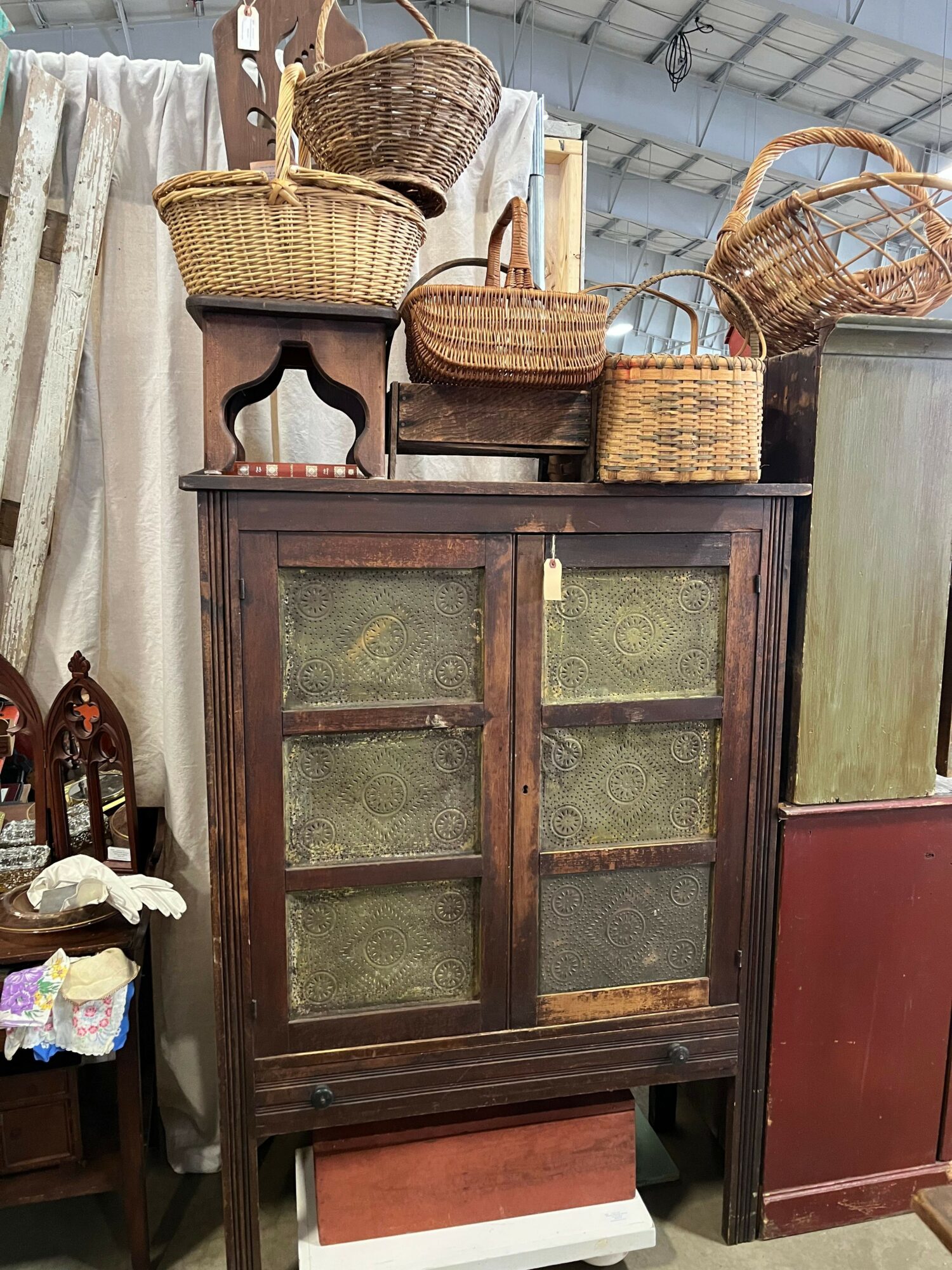 Wooden cabinet with glass panels, surrounded by wicker baskets and chairs, with a small table and decorative items nearby.
