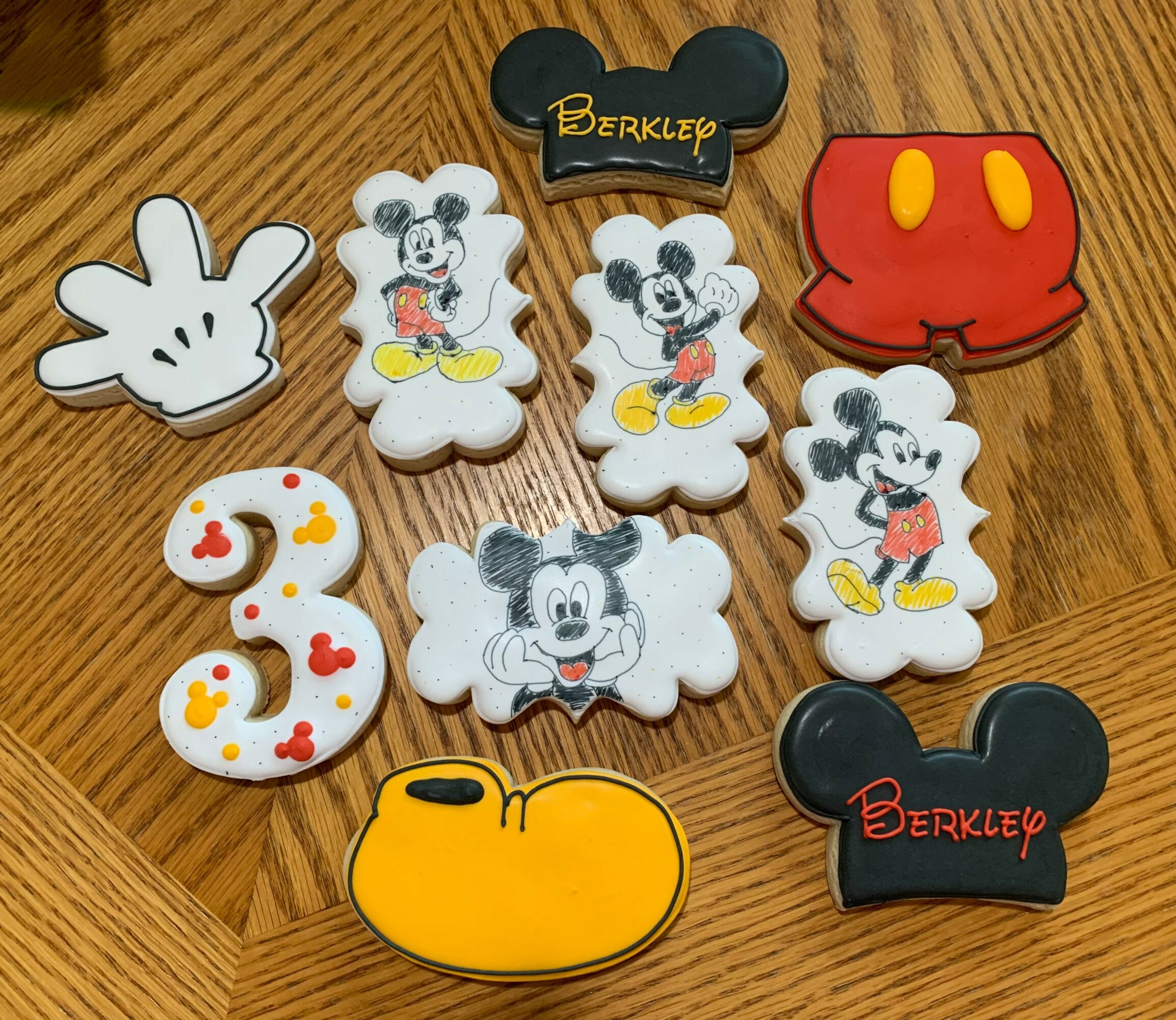 Collection of Mickey Mouse-themed patches and accessories on a wooden surface, including Mickey faces, gloves, and shoes, with some featuring the Berkley brand. Word 'Berkley' appears on two items.