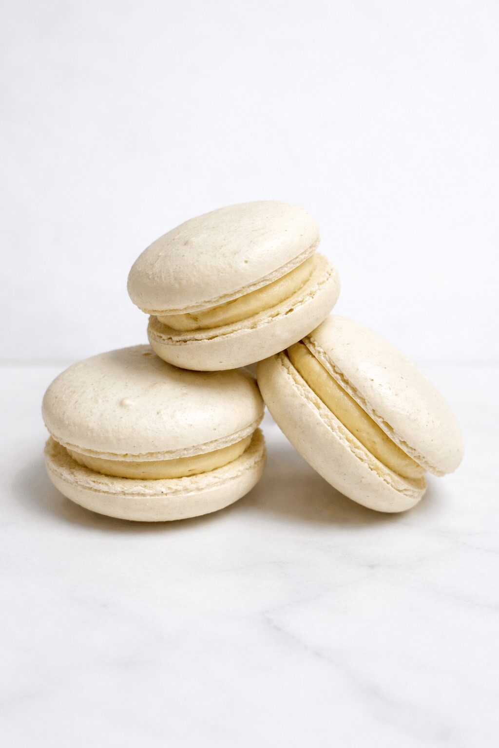 Four white macarons stacked on a white surface with a plain white background.