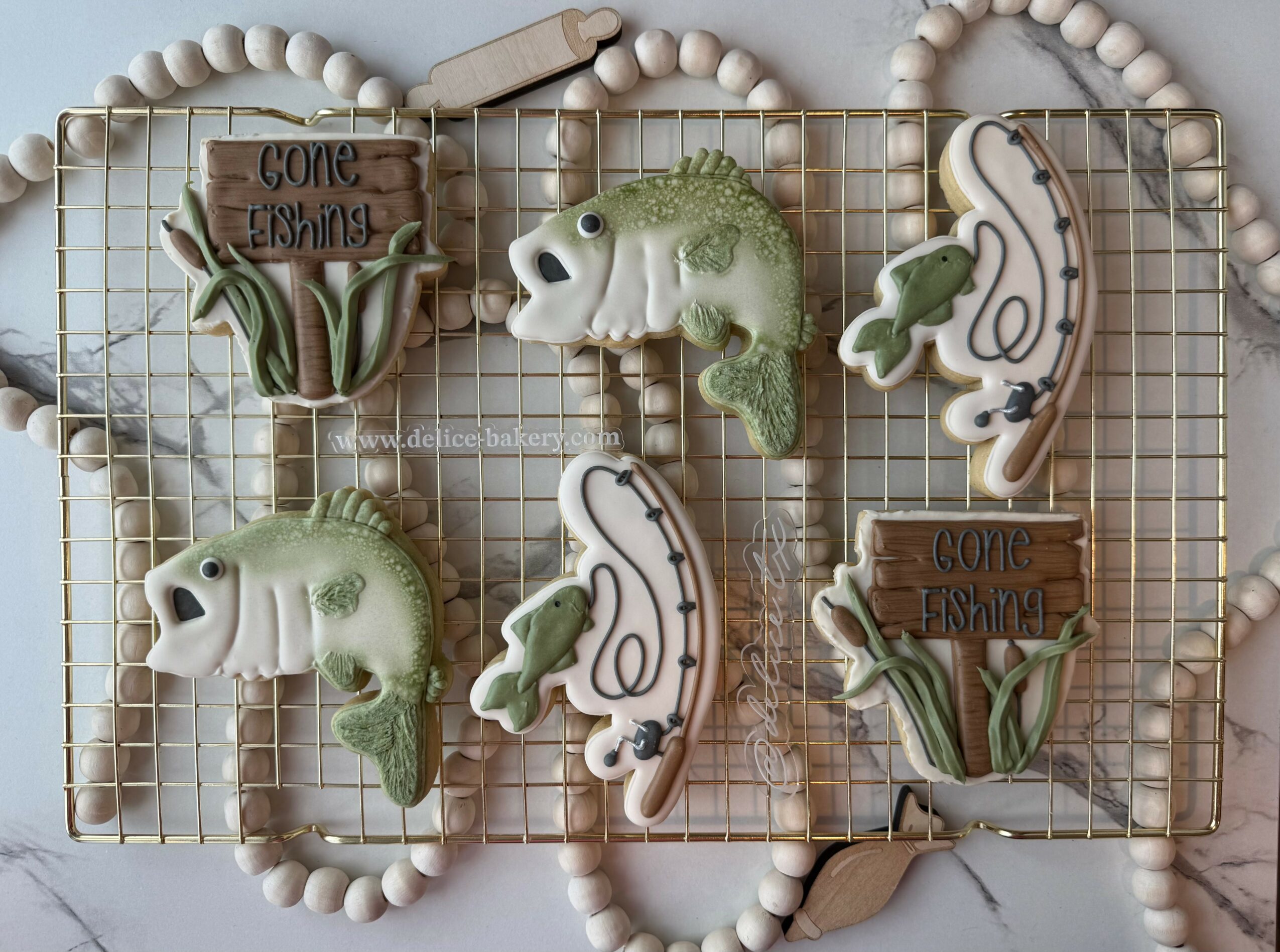 Decorative cookies shaped like fish, chameleons, and plants on a wire grid with beaded border, with signs reading 'Come Fishing'.