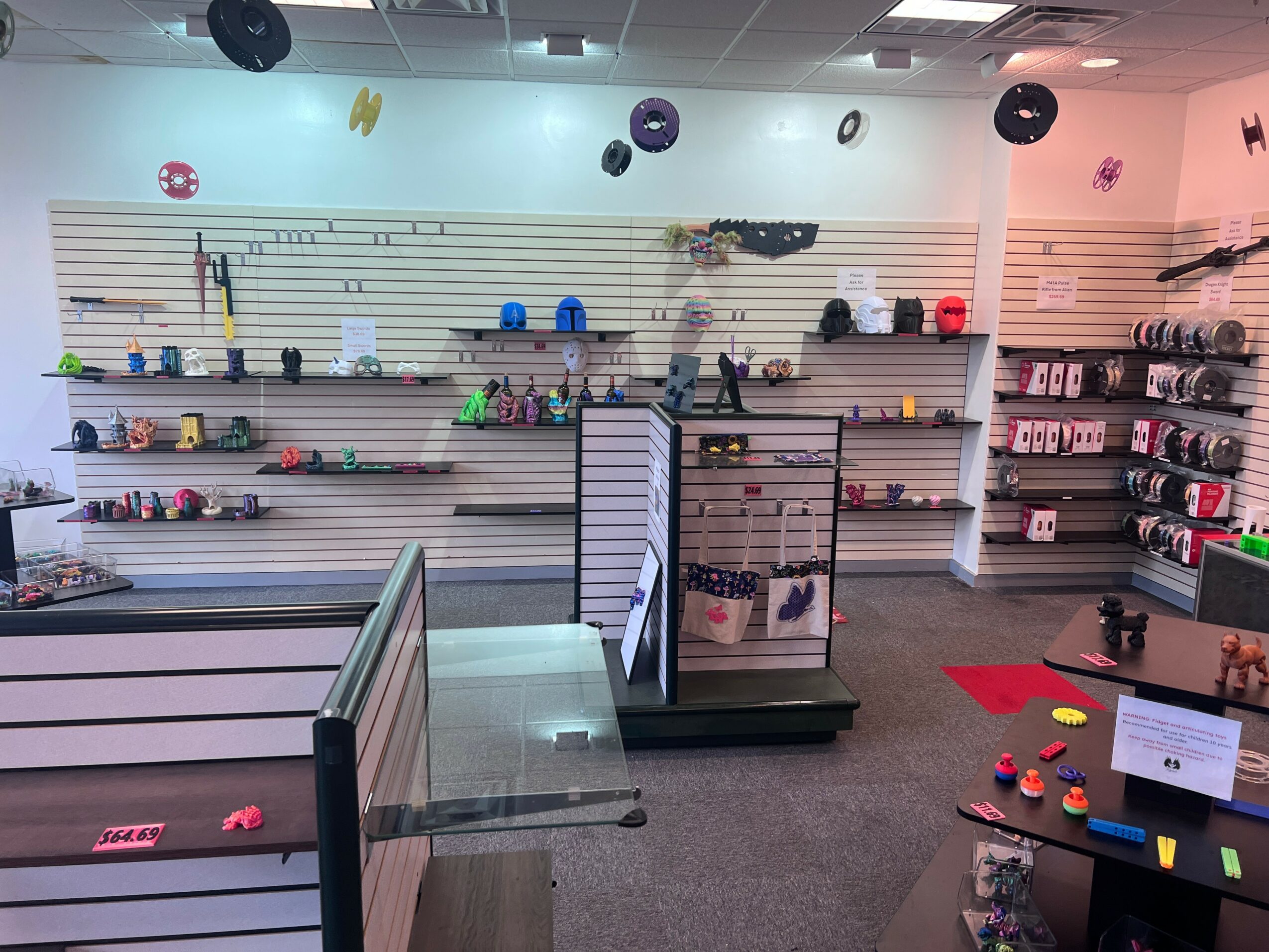 Store interior with shelves displaying various products, a checkout counter, and a gray carpeted floor.