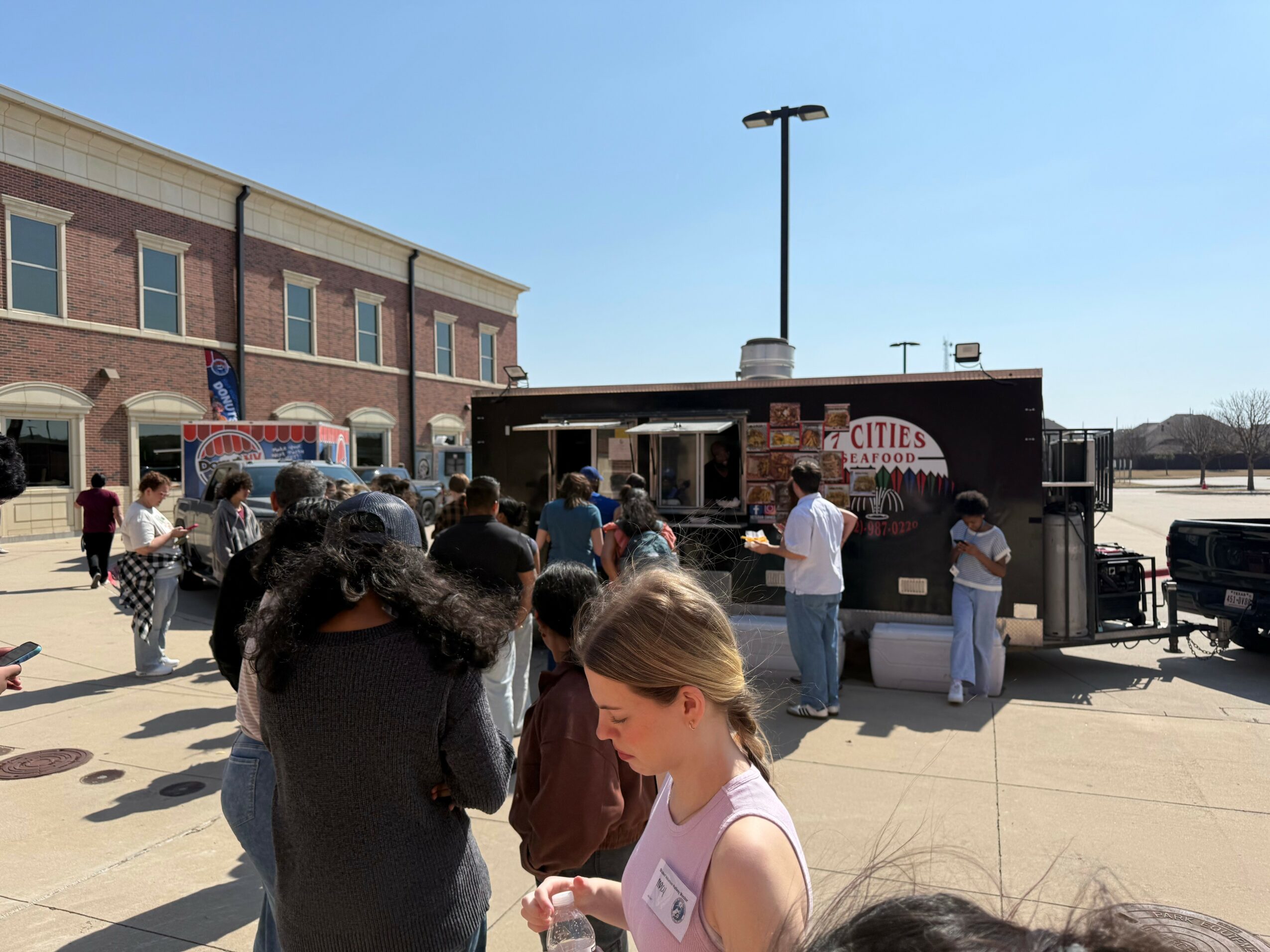 People gather outside a food truck with a sign that reads 'City' on a sunny day.