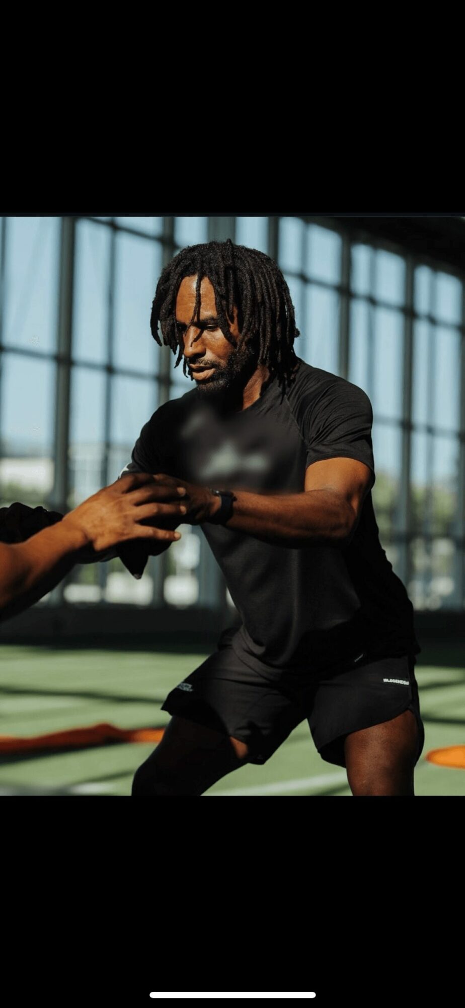 Person with dreadlocks practicing a martial arts move indoors, with large windows in the background.