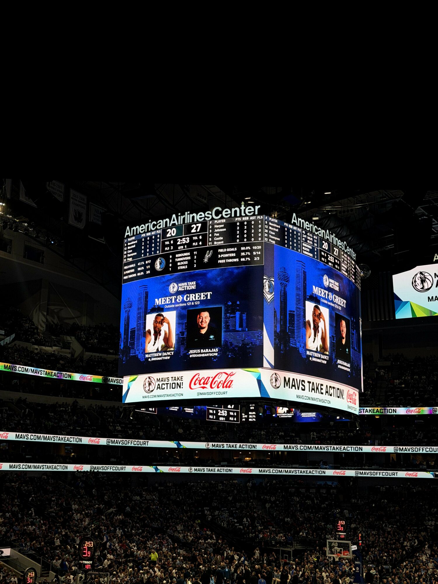 Indoor sports arena with large digital scoreboard displaying scores and advertisements, filled with spectators, ceiling and banners visible.
