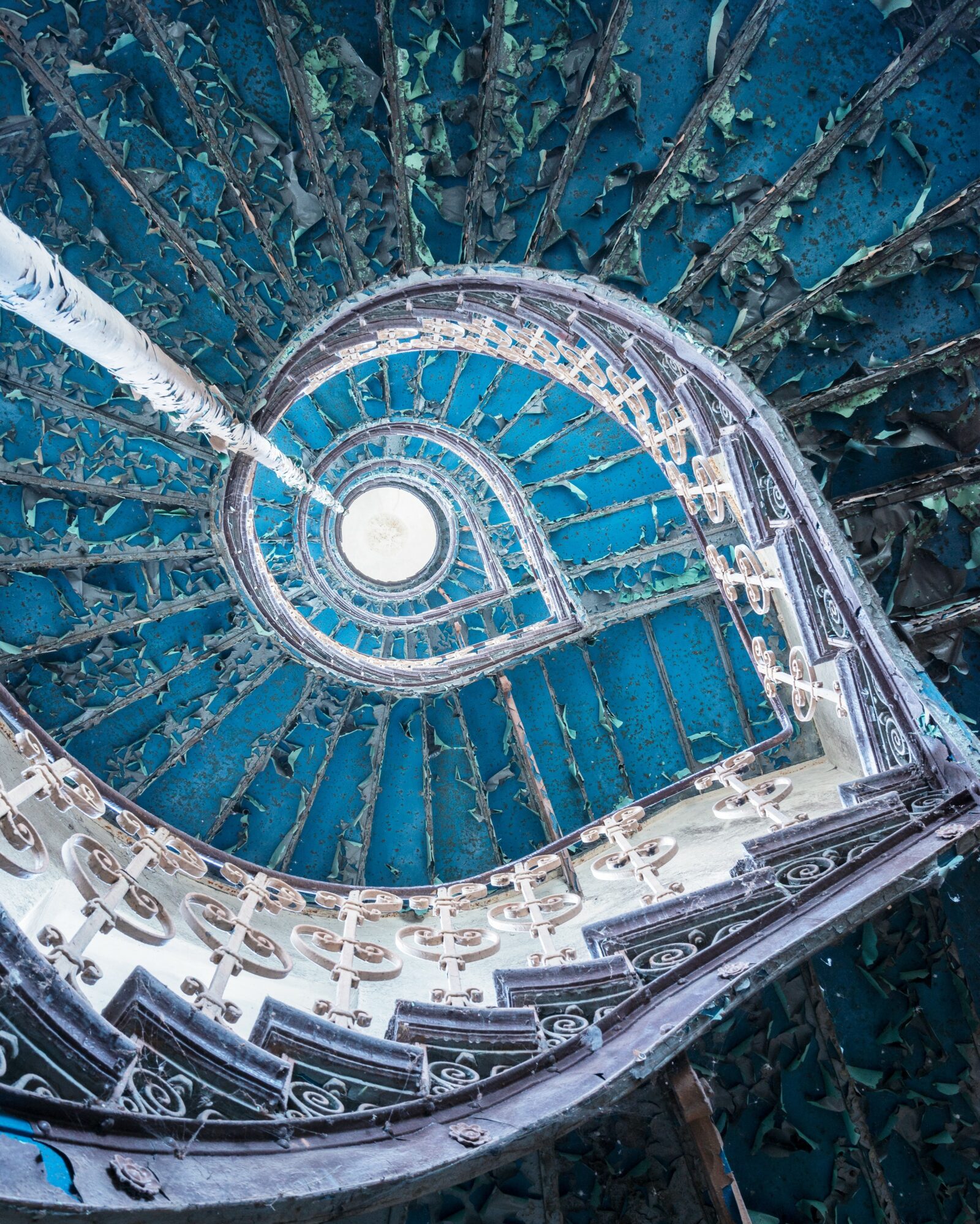 Spiral staircase viewed from above, with transparent sides and blue steps, descending into darkness.