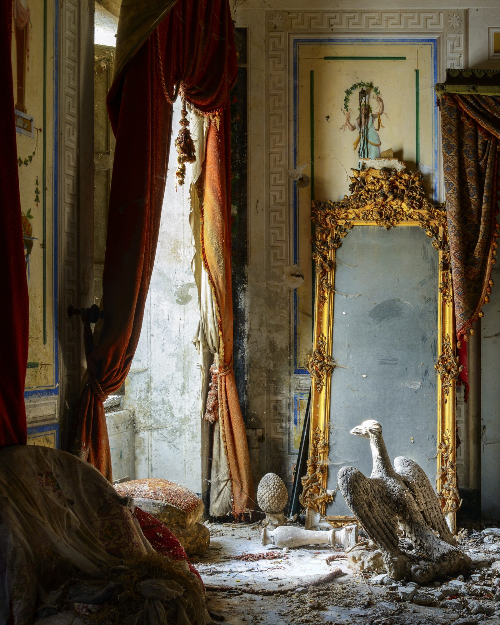 Interior with ornate gold mirror, tall window with red curtains, and decorative wall art, sunlight streaming in.