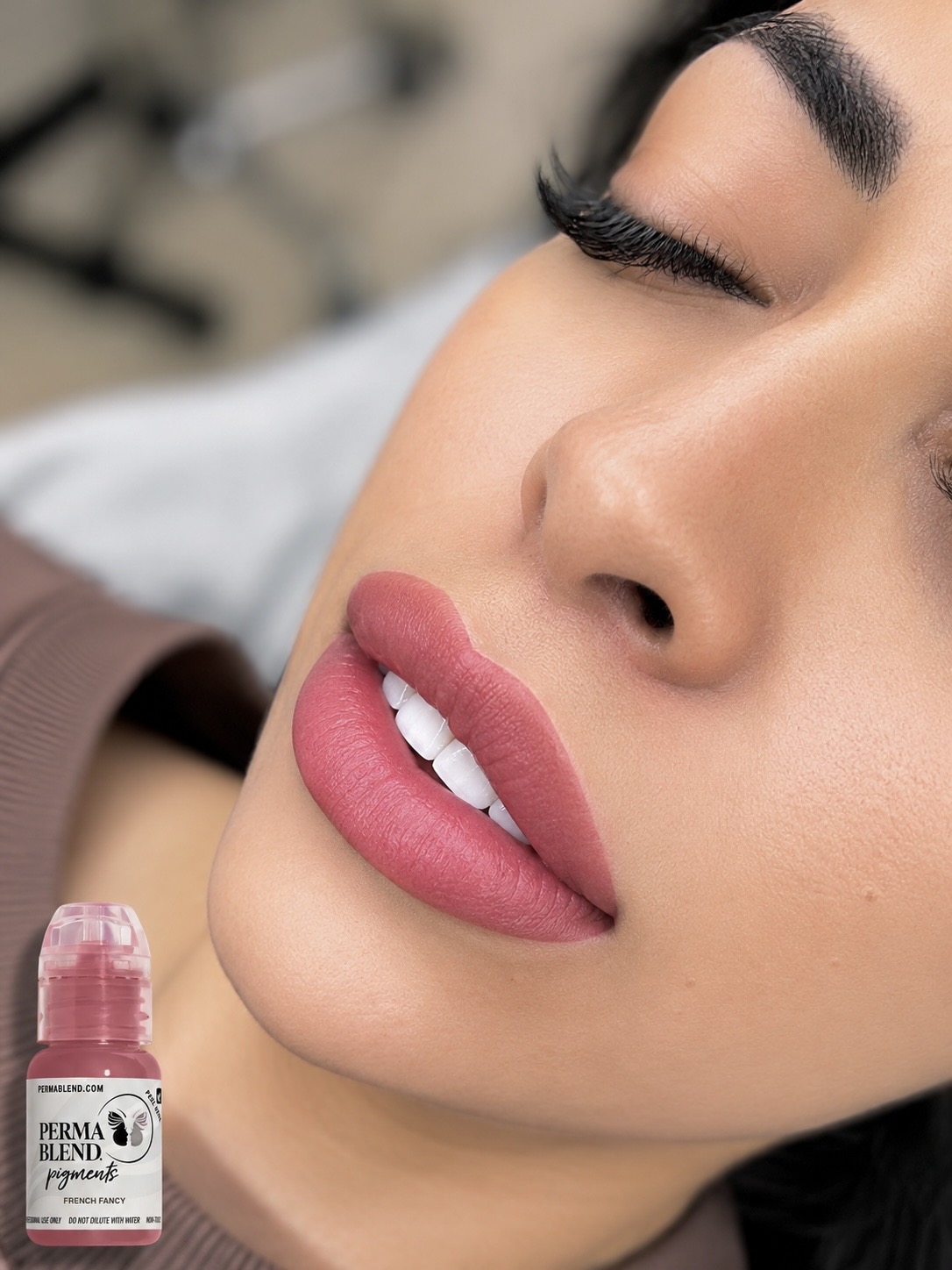 Close-up of a woman's face with makeup, closed eyes, and pink lipstick, holding a lip gloss tube.