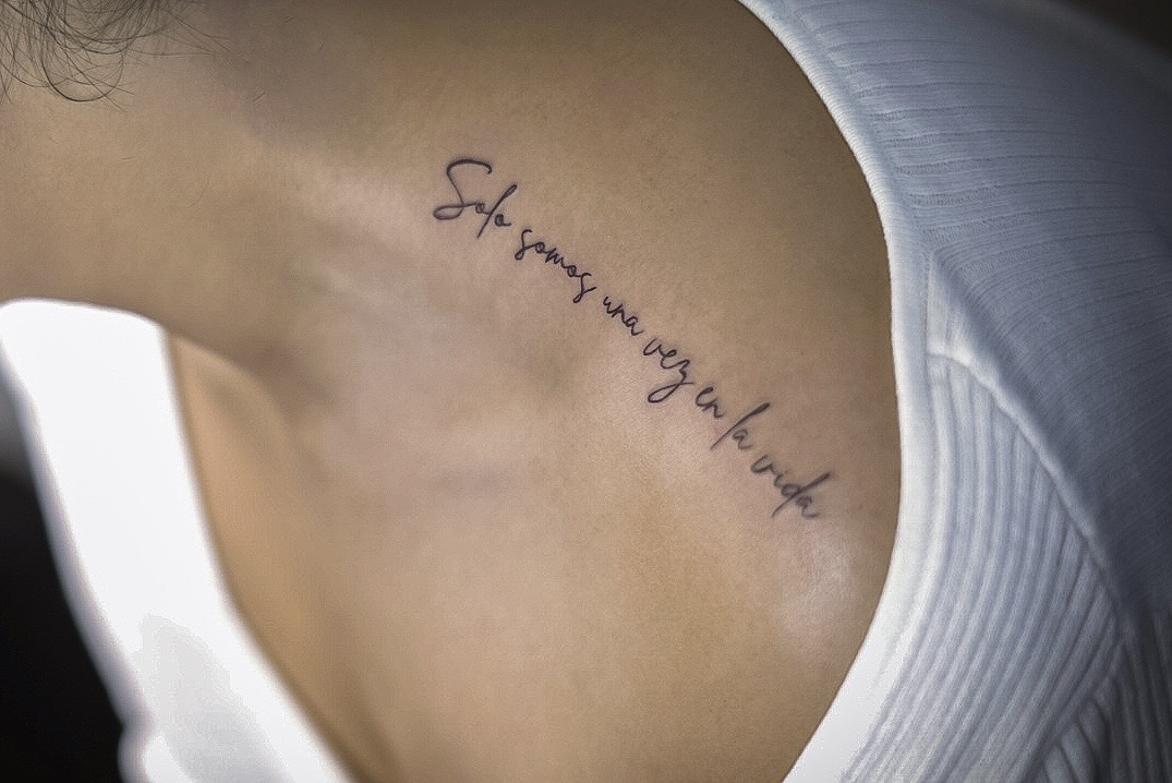 Tattoo on person's upper chest with text in cursive script, partially visible, next to white clothing.