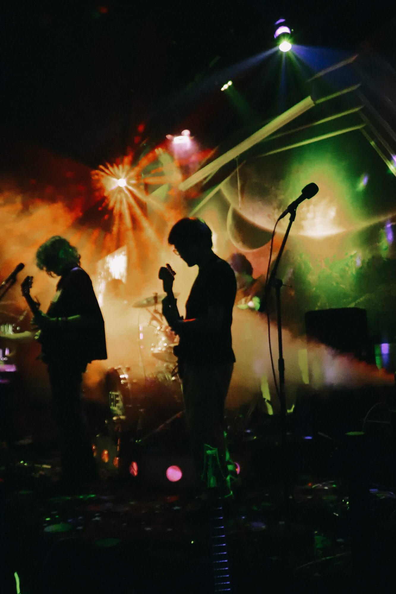 Silhouettes of musicians performing on stage with colorful lights and smoke effects, microphone stand in foreground.