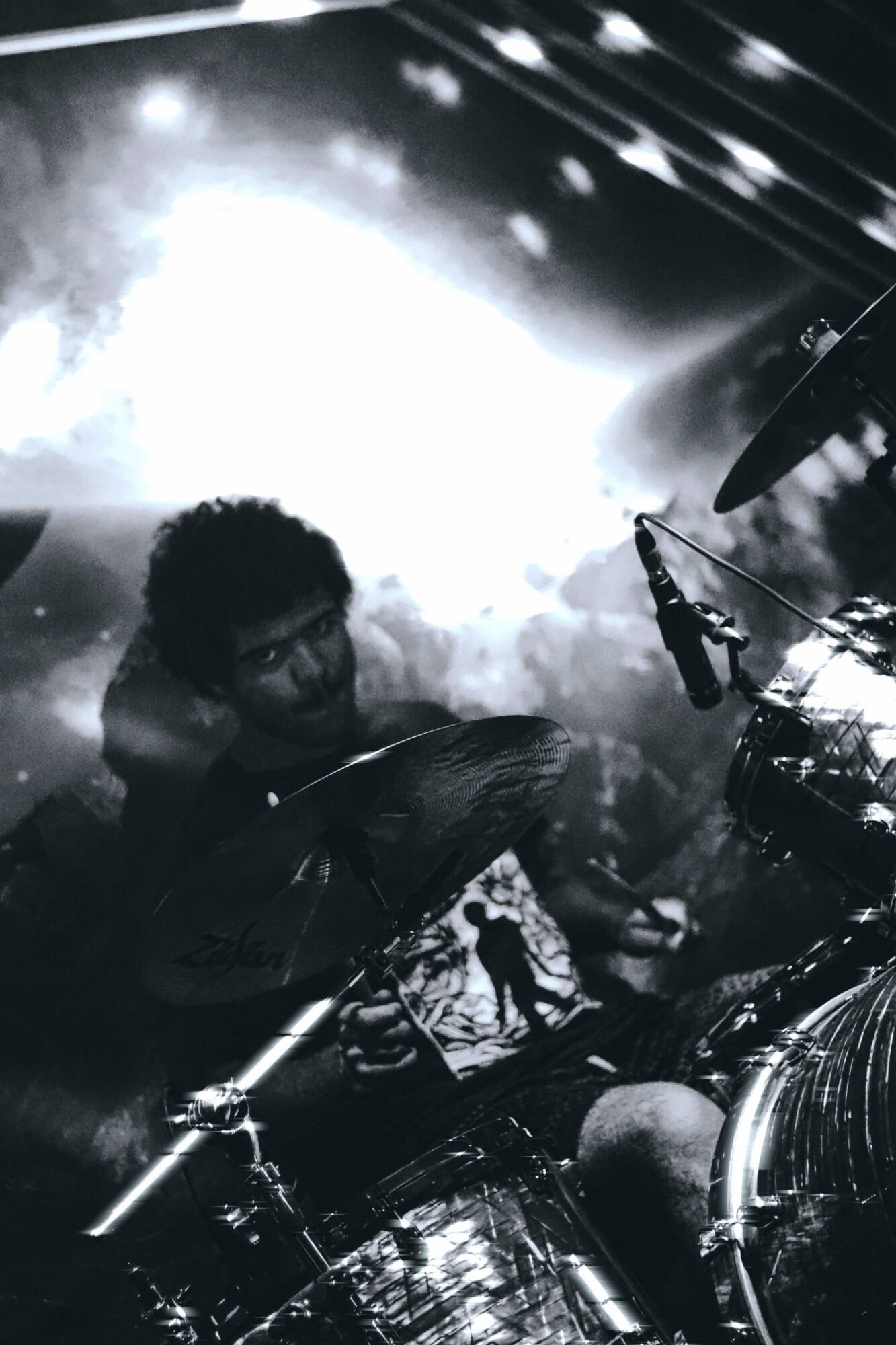 A person playing drums on stage with bright lights and smoke effects in the background.