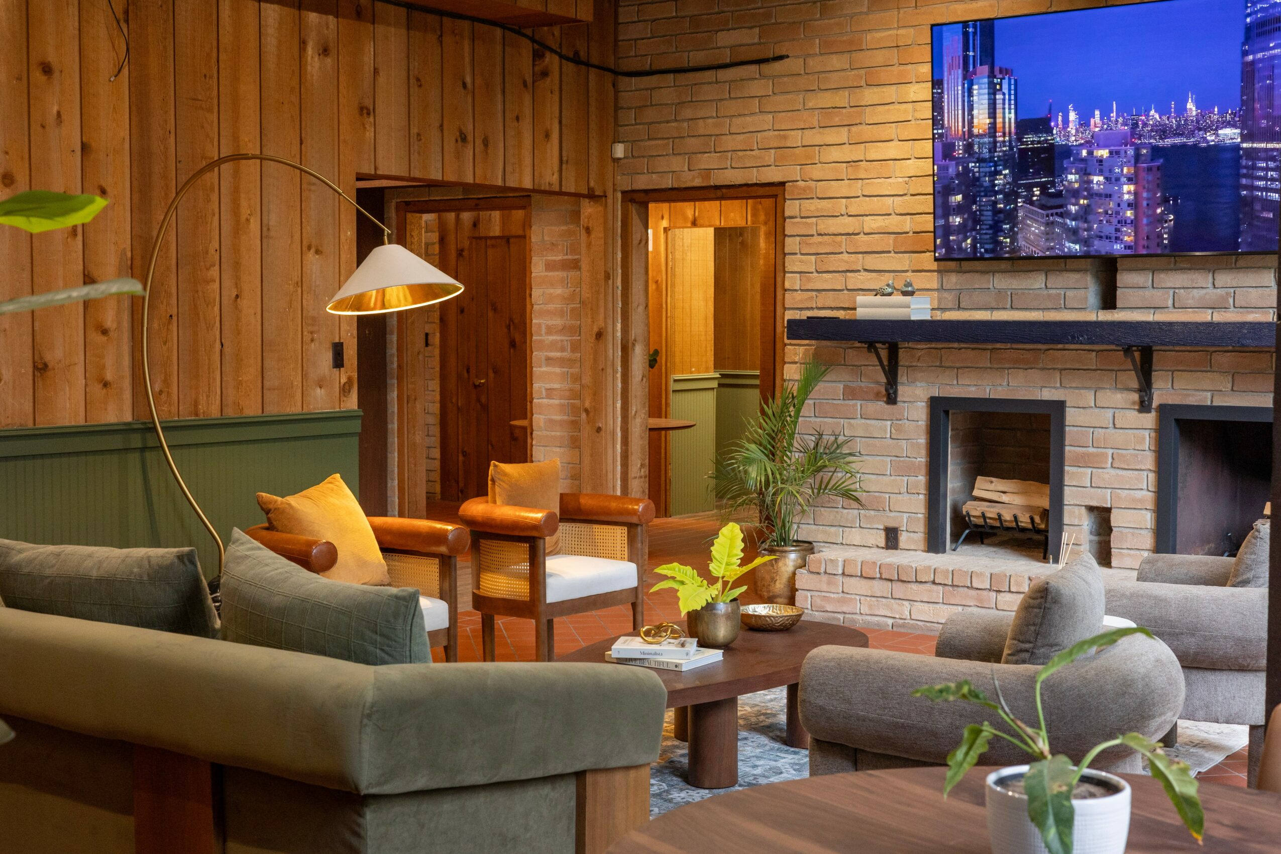 Living room with wooden walls, a fireplace, a wall-mounted TV, and various chairs and plants.