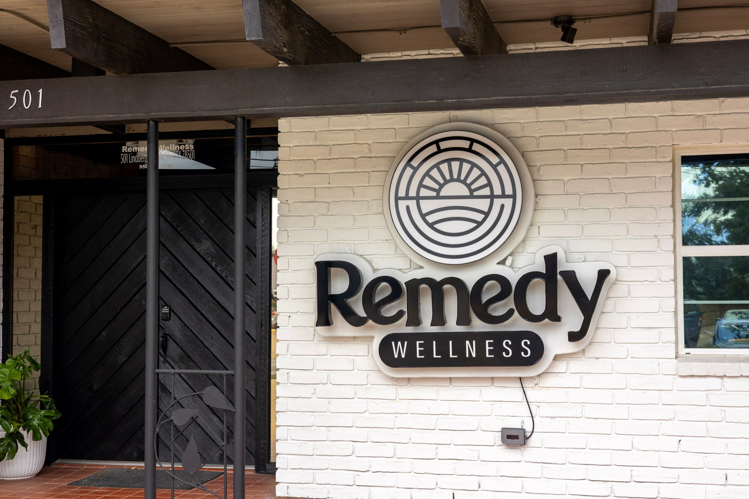 White brick wall with a circular logo and the words 'Remedy Wellness' in black, with a window on the right.