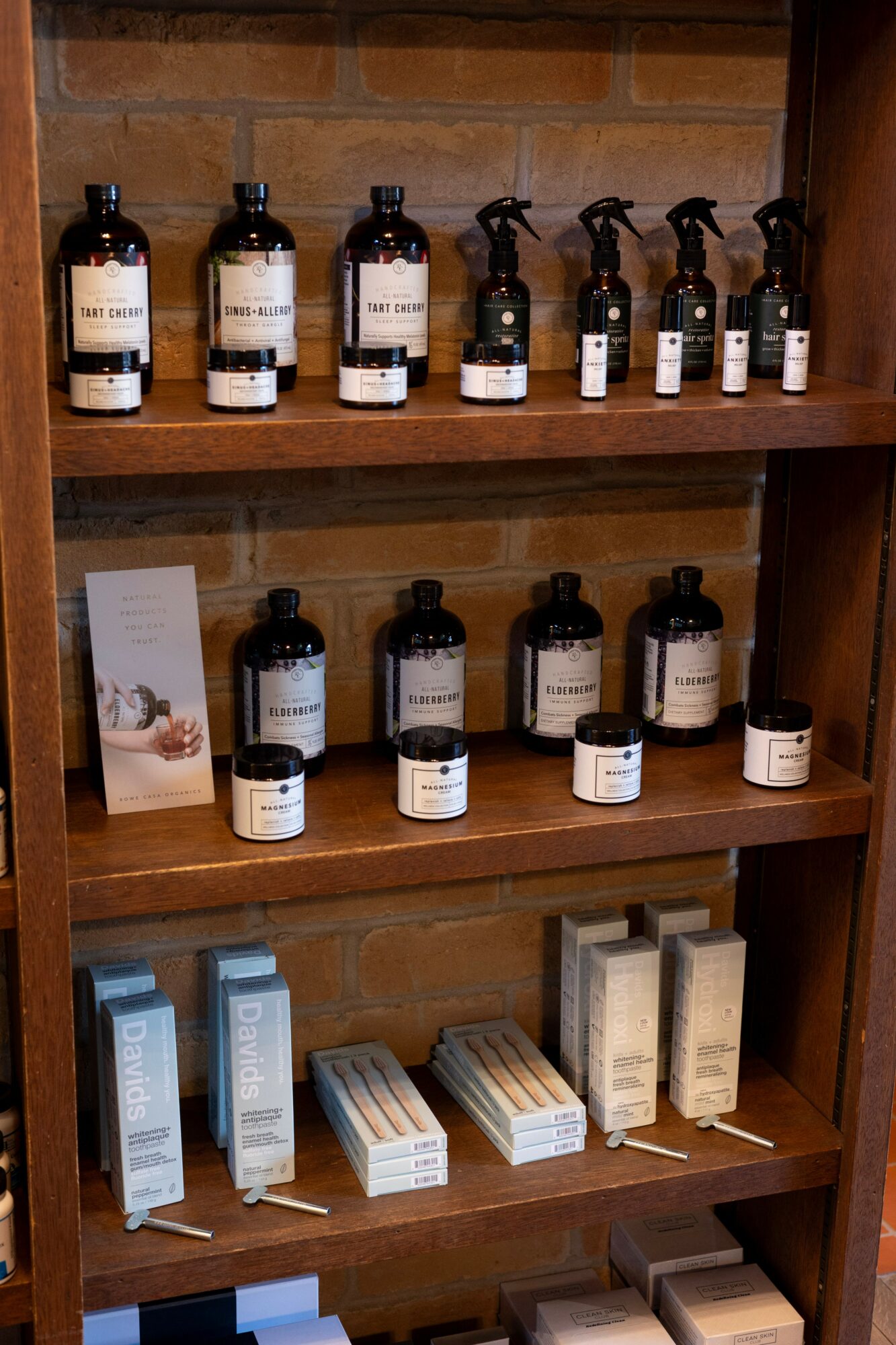 Wooden shelf with bottles of skincare products, boxes, and a small sign, arranged on three shelves.