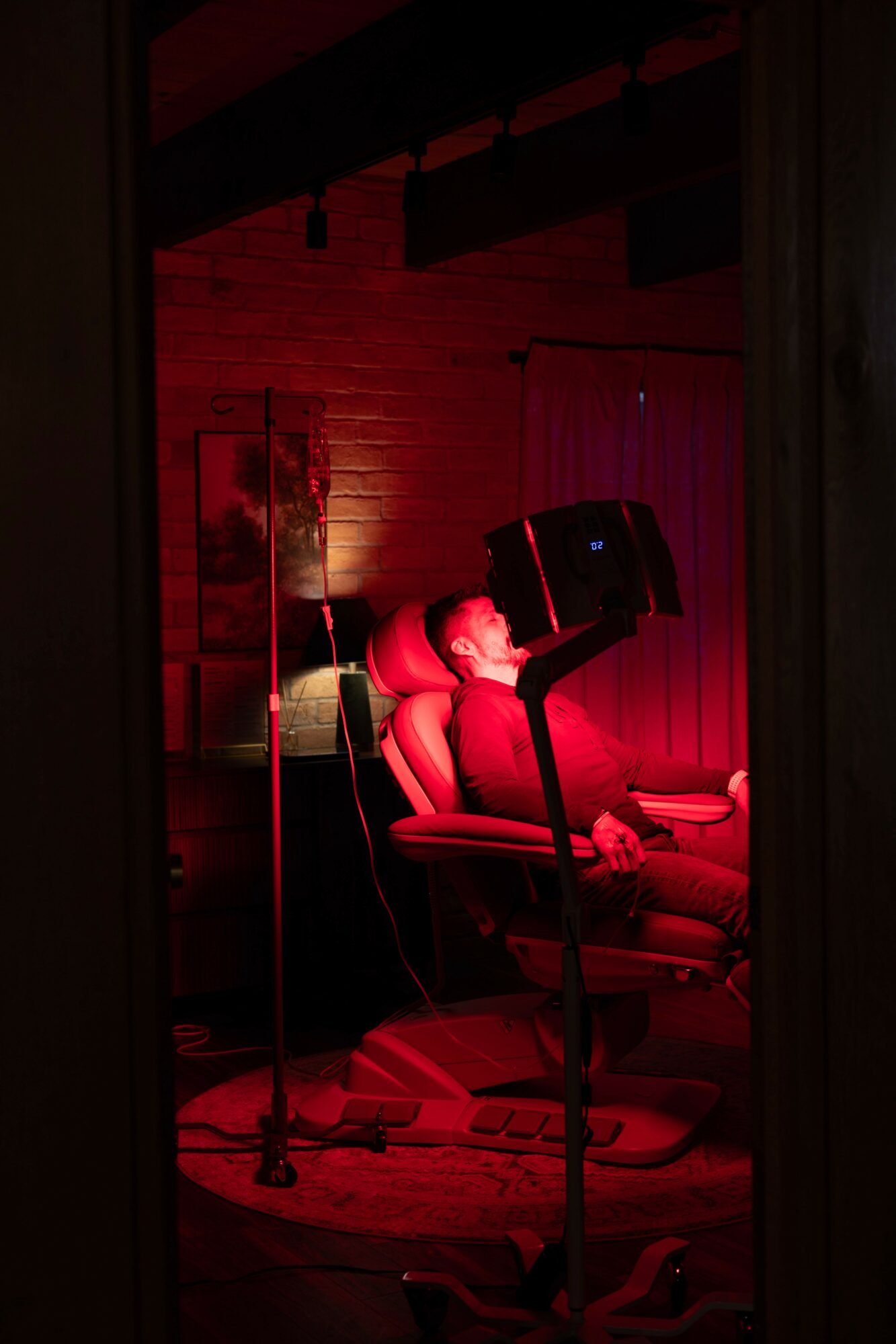 Person sitting in a chair on a stage with red lighting, surrounded by microphones and equipment.