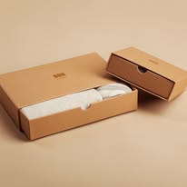 Open cardboard box with white fabric inside, next to a closed box on a beige surface.