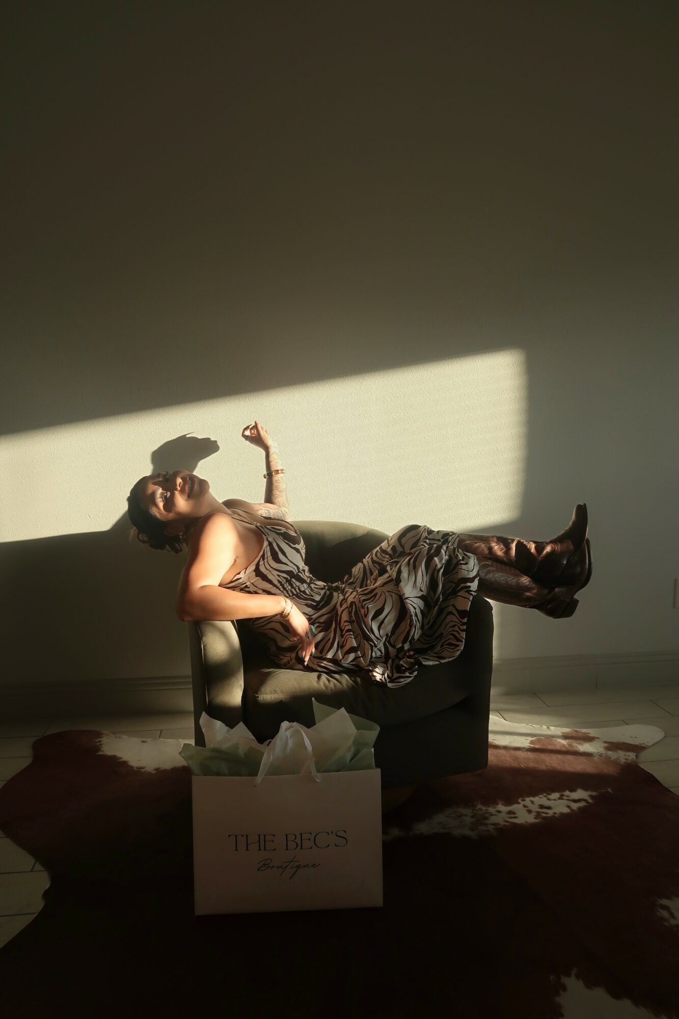 Person lying on a sofa with legs up, holding a phone, illuminated by sunlight through a window, with a box in front.