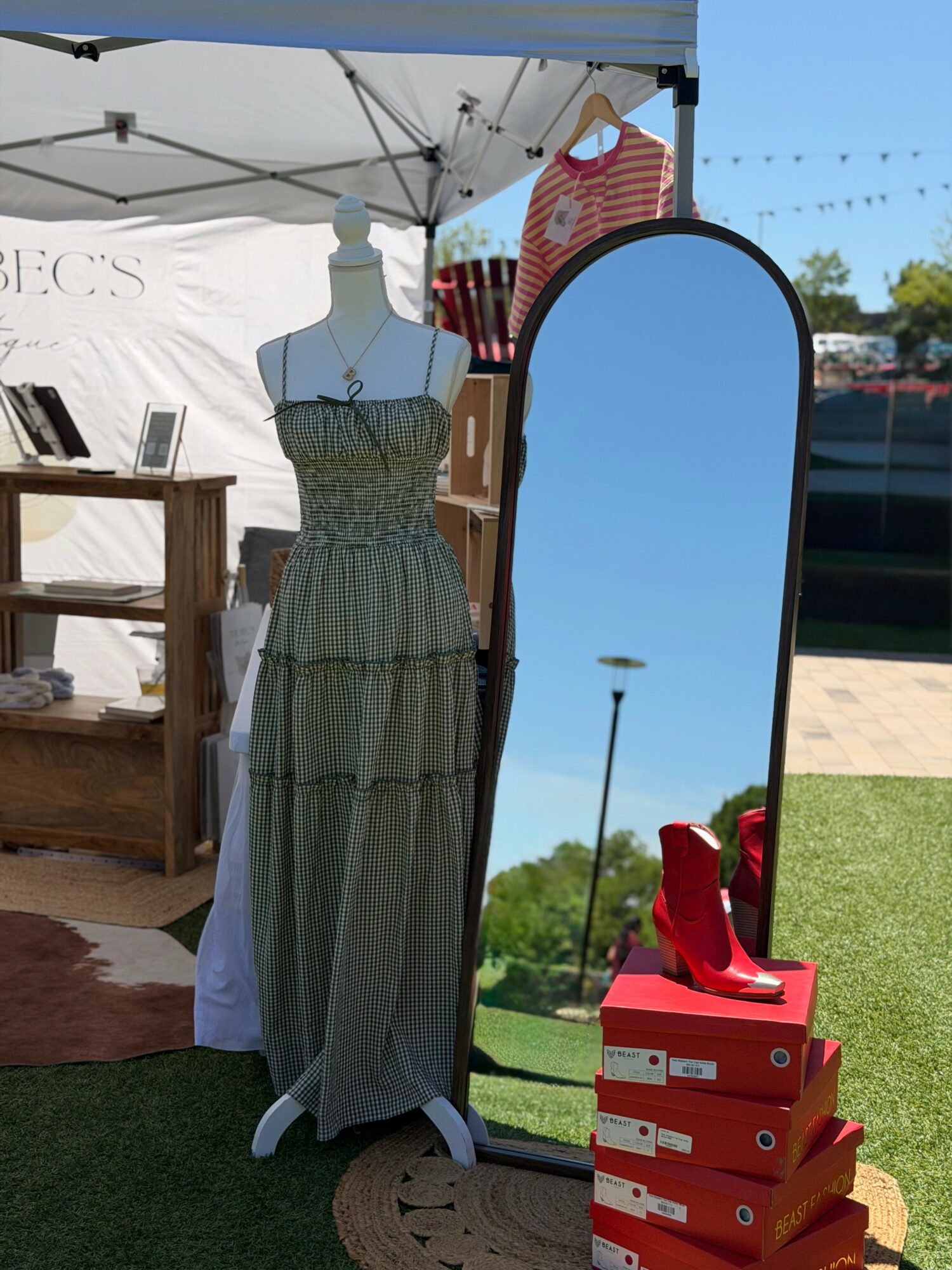 Mannequin wearing a striped dress, standing in front of a mirror outside at a market stall with shoes on a stack of boxes.