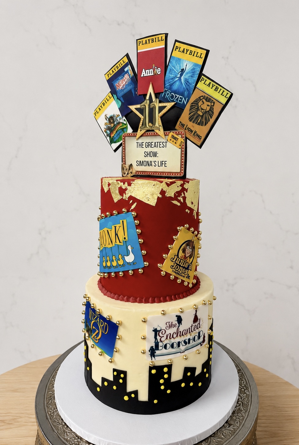 Two-tiered cake with comic book and superhero decorations, featuring a star topper and colorful paper signs on top, on a white cake board.