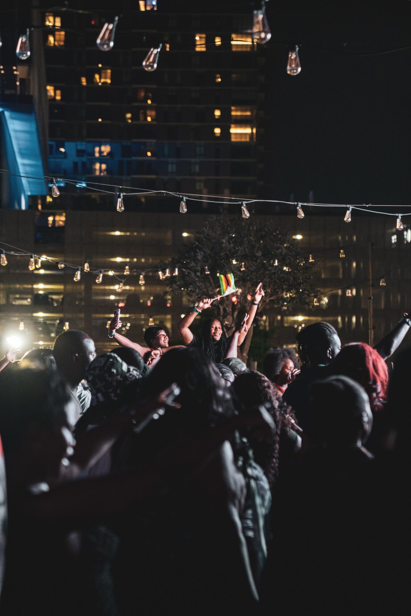 Crowd of people at night with city lights and hanging bulbs in the background.