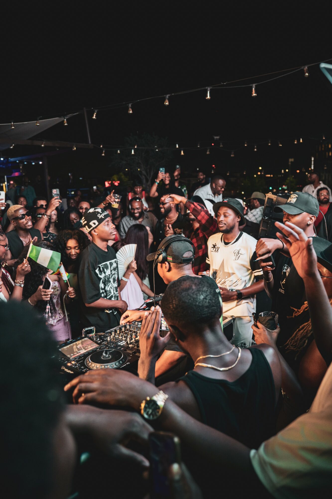 Crowd of people dancing and socializing at a nighttime party with string lights overhead.