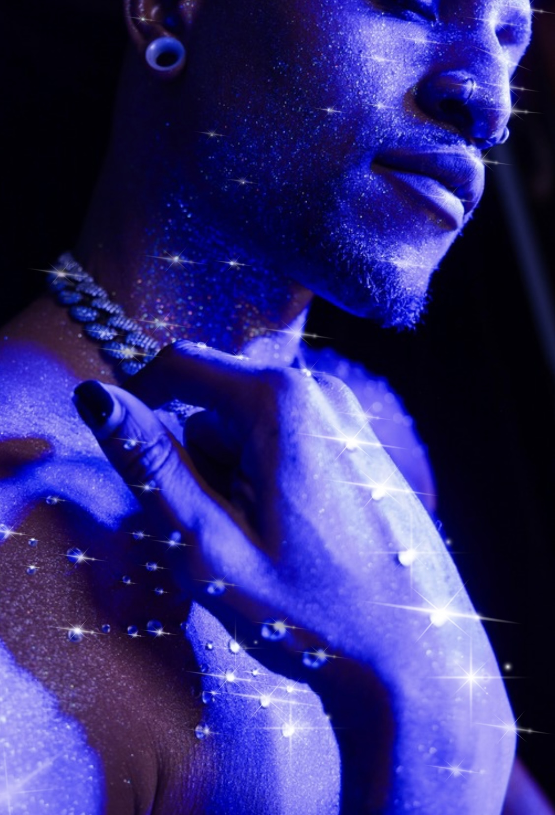 Close-up of a person with glowing blue paint and jewelry, hand near neck, dark background, star-like effects.