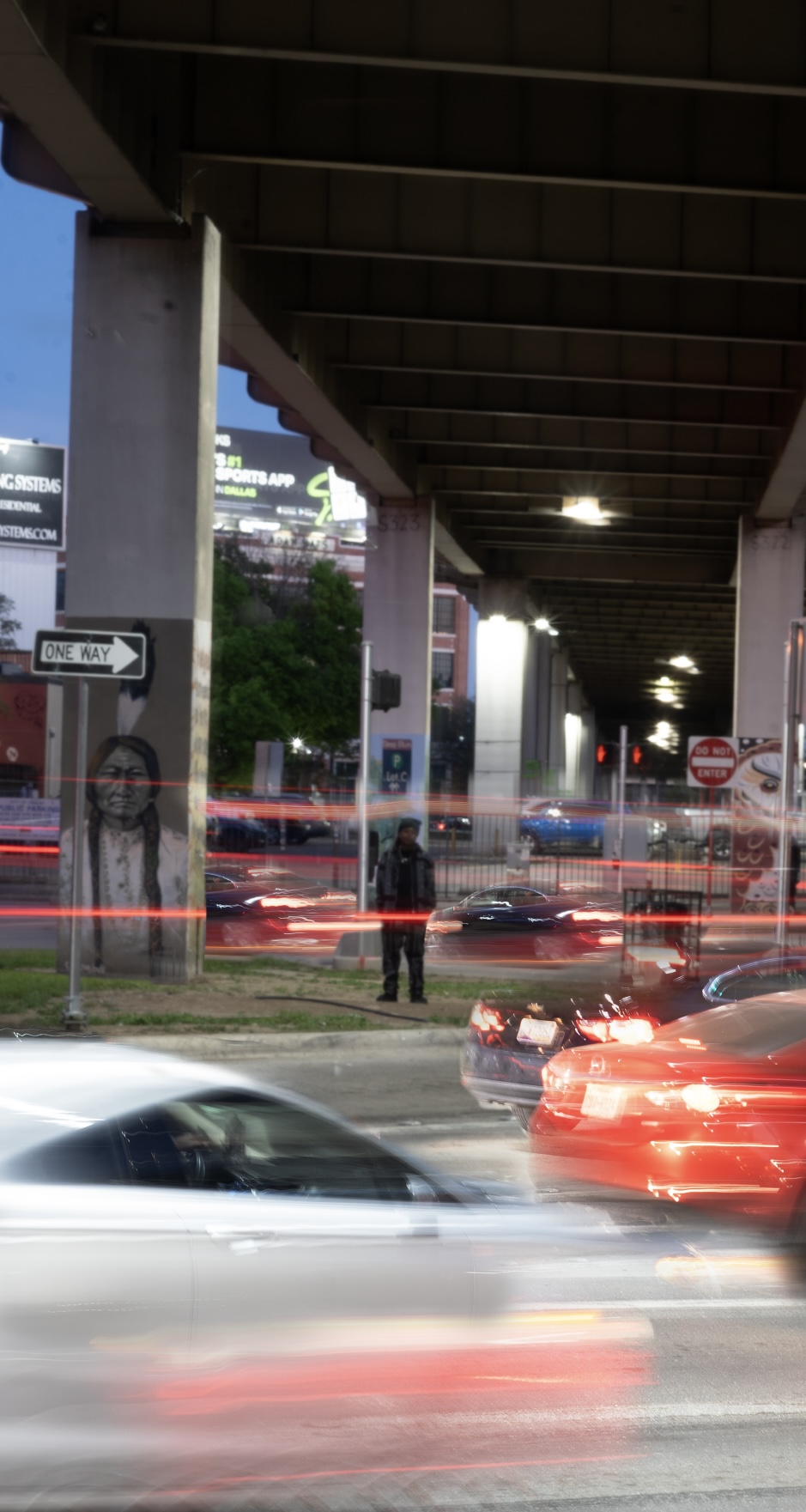 Underpass with cars passing by, light trails from moving vehicles, and a person standing near the sidewalk.