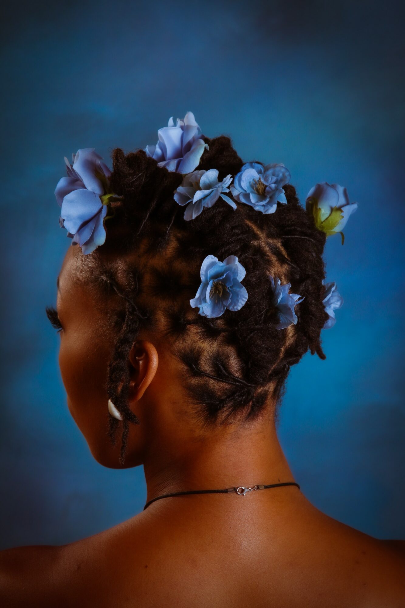 Back of a woman with braided hair decorated with blue and white flowers, against a dark background.