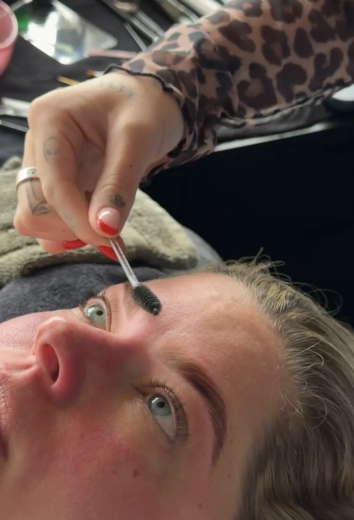 Person with blue eyes and blonde hair receives a cosmetic treatment on their nose using a small tool, in a close-up view.