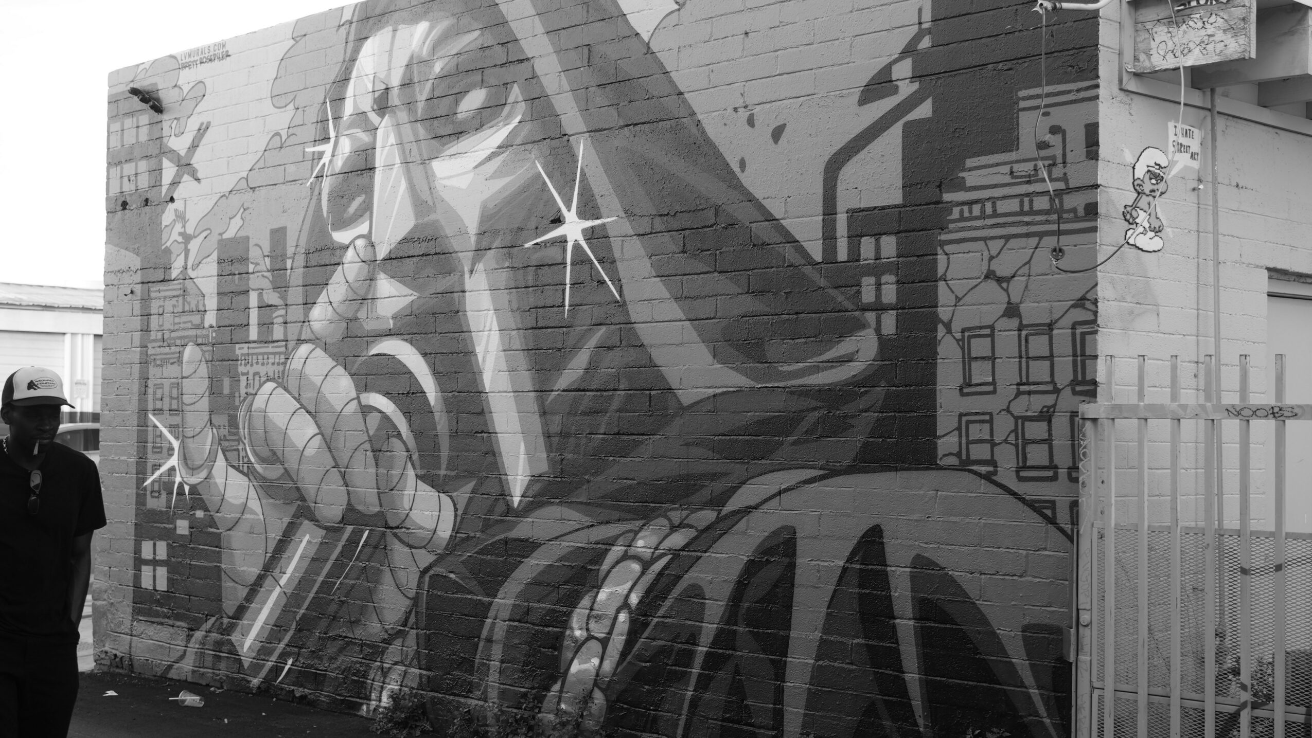 Street mural of a large robotic figure with cityscape background, person standing nearby, black and white image.