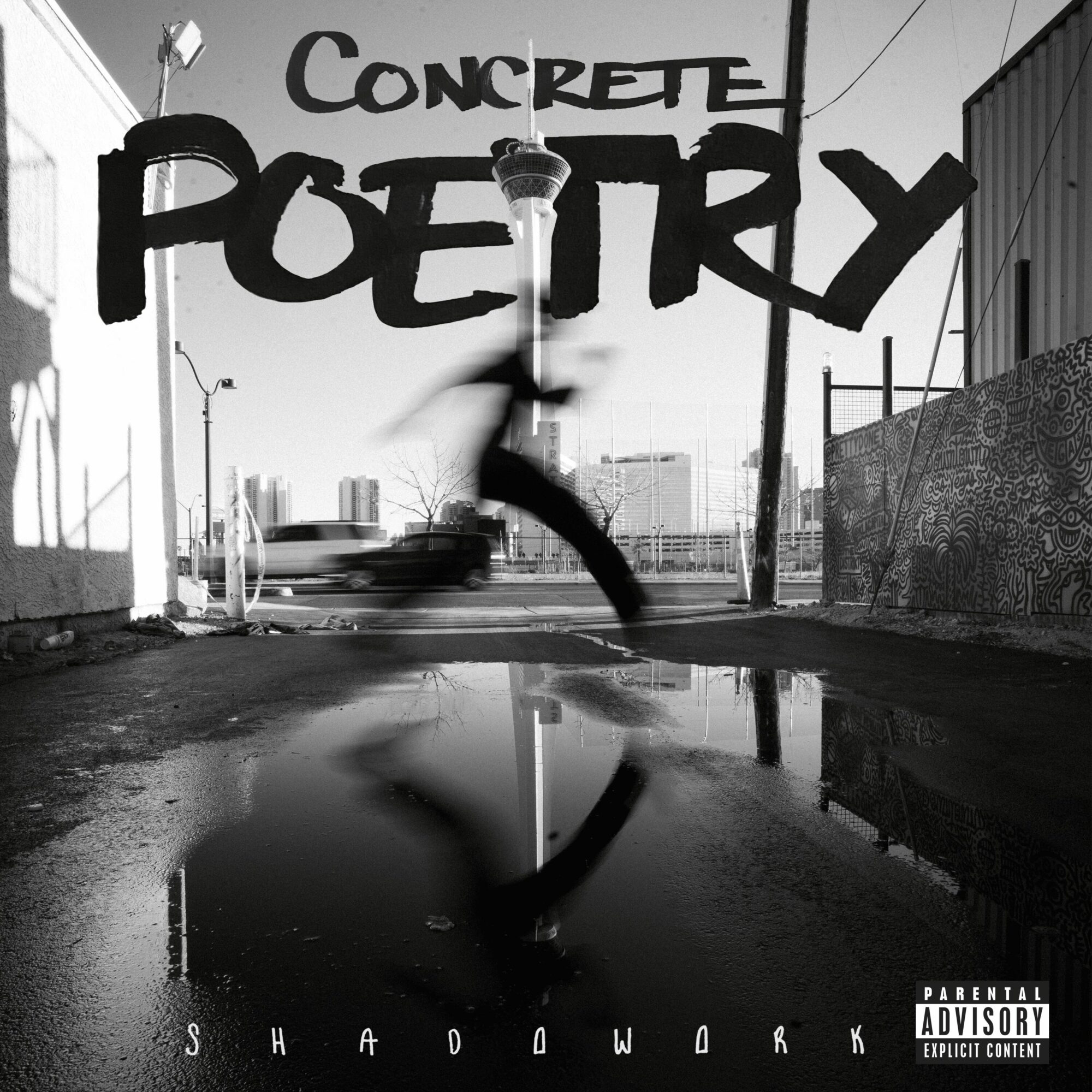Street scene with graffiti reading 'CONCRETE POETRY' and a blurred person jumping, reflected in a puddle, in black and white.