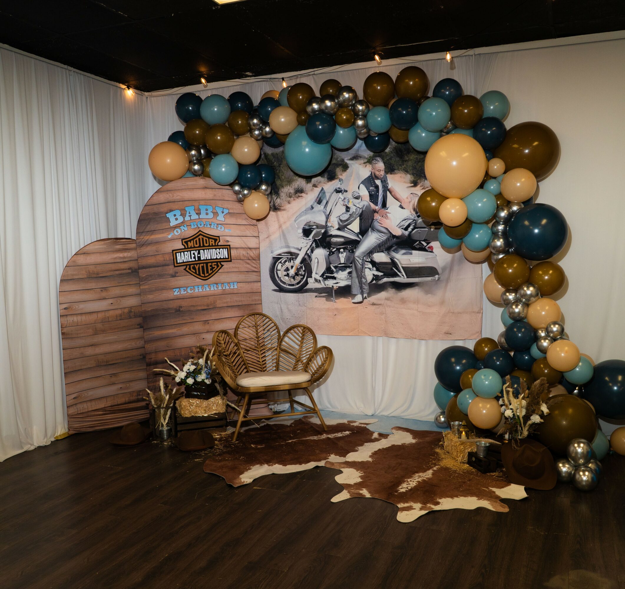Decorative Harley-Davidson themed display with balloons, a wooden backdrop, a chair, and a cowhide rug.