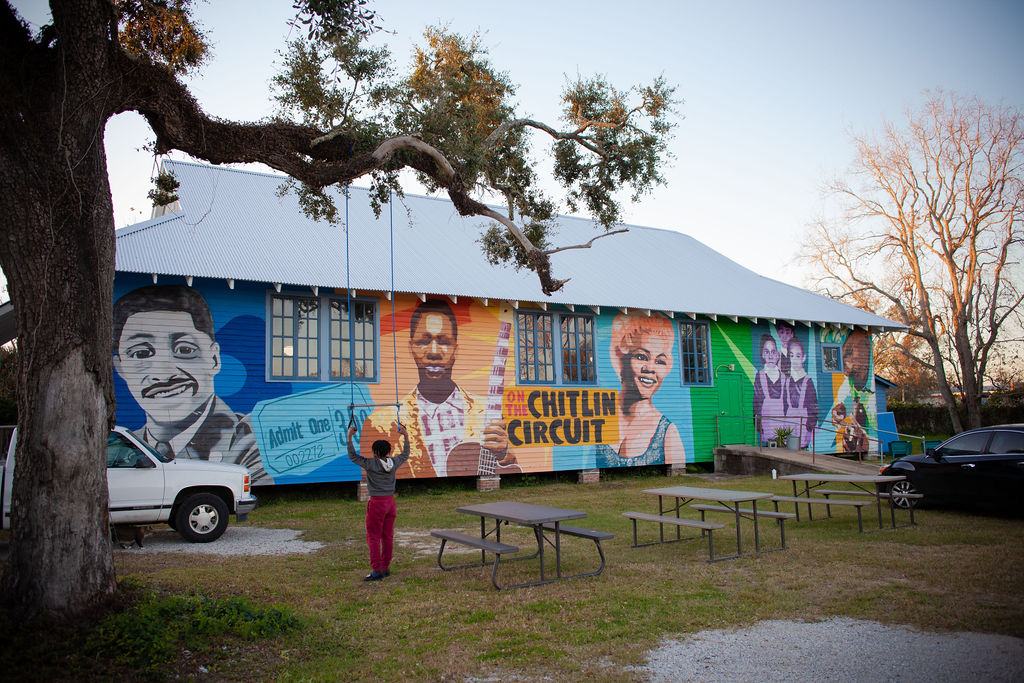Colorful mural on building wall featuring children and text, with a person standing in front and trees nearby.
