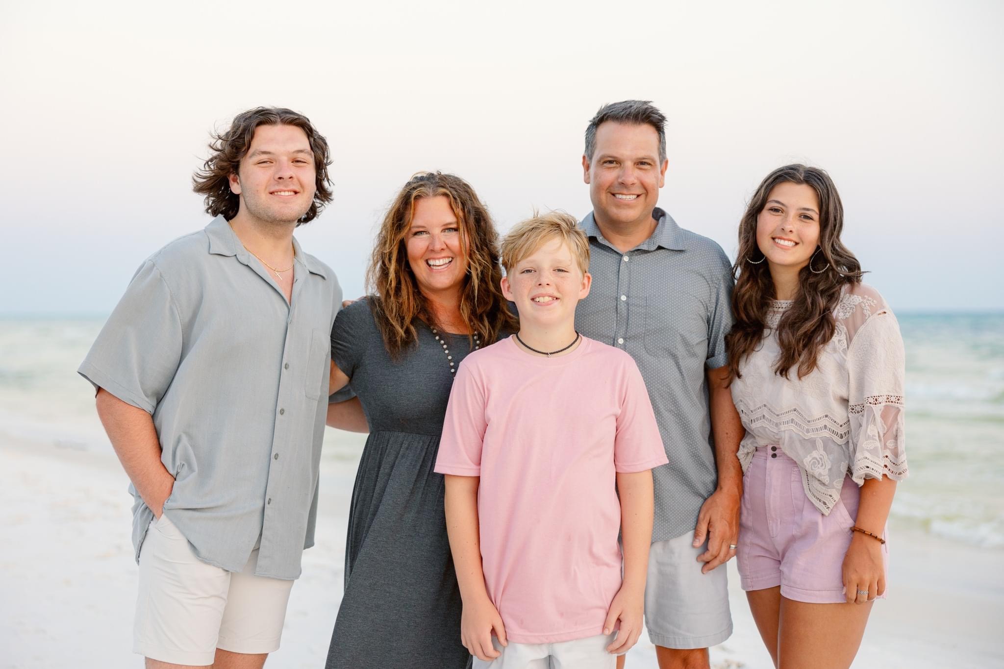 Family of five standing on the beach, smiling, with ocean waves in the background.