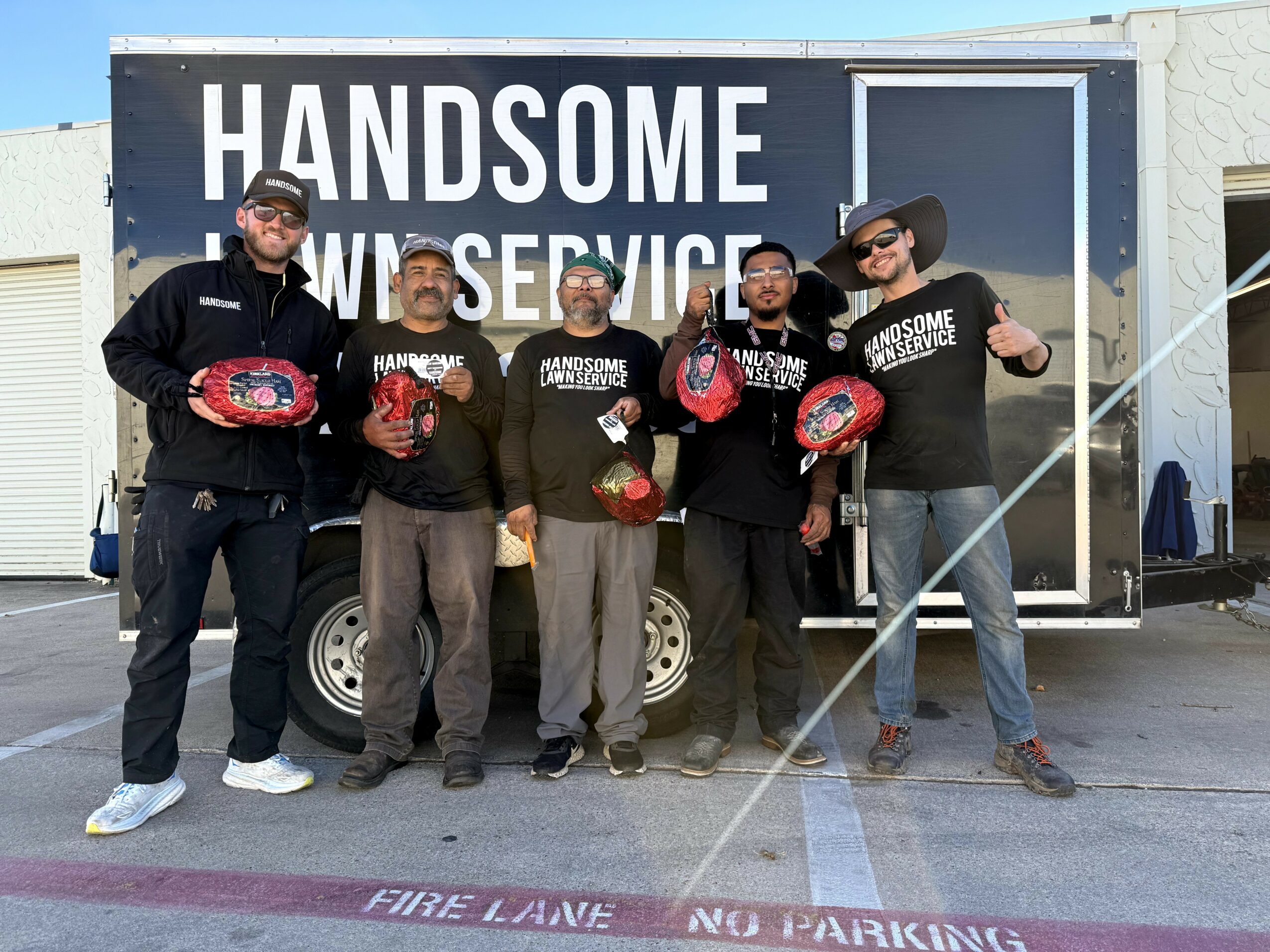 Group of five people standing in front of a mobile service trailer, holding red helmets, smiling, with a sign reading 'HANDSOME WINDSERVICE' behind them.
